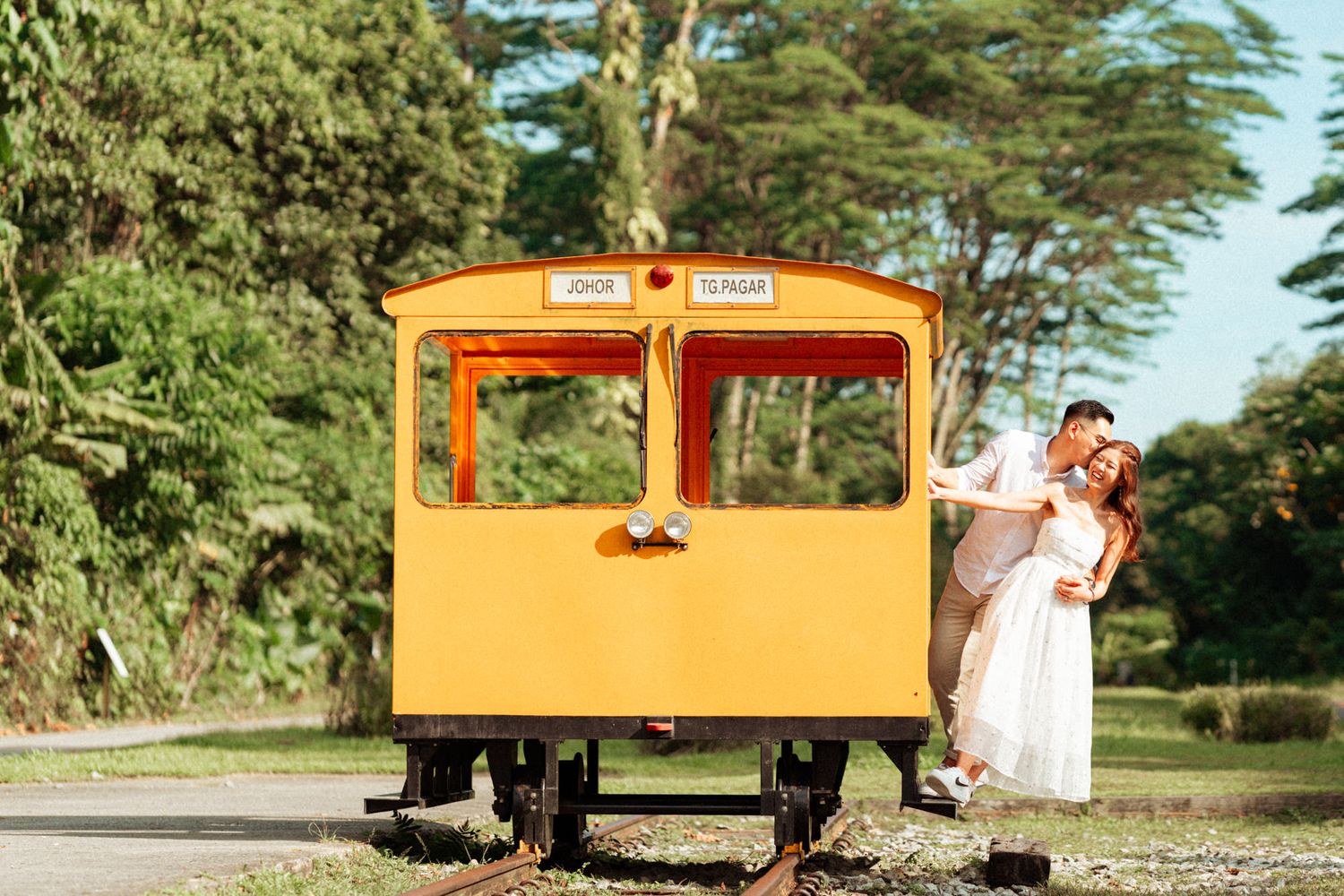 Bright orange vintage train car set against lush tropical greenery in outdoor setting.
