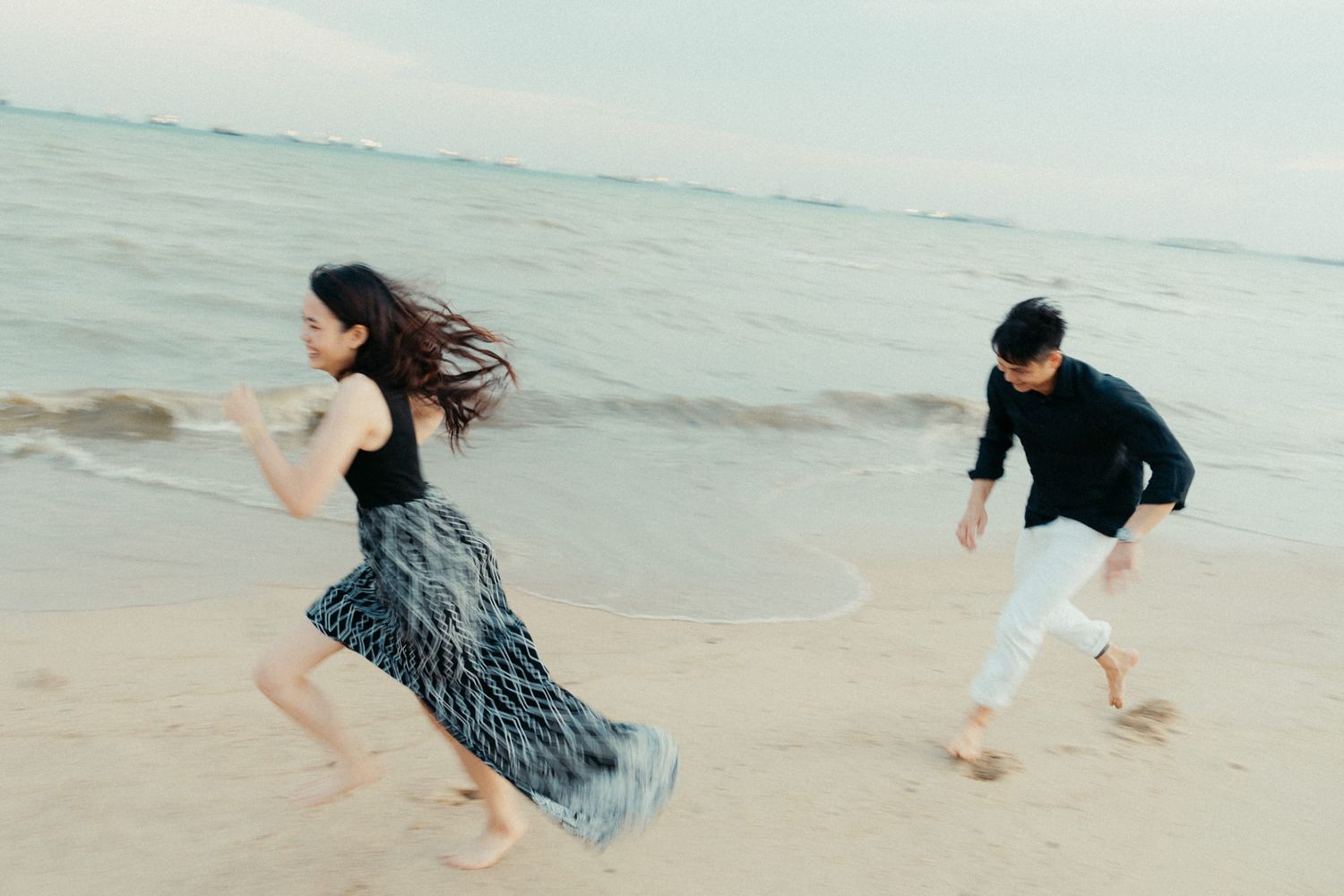 Playful couple running and splashing along the shoreline at the beach.