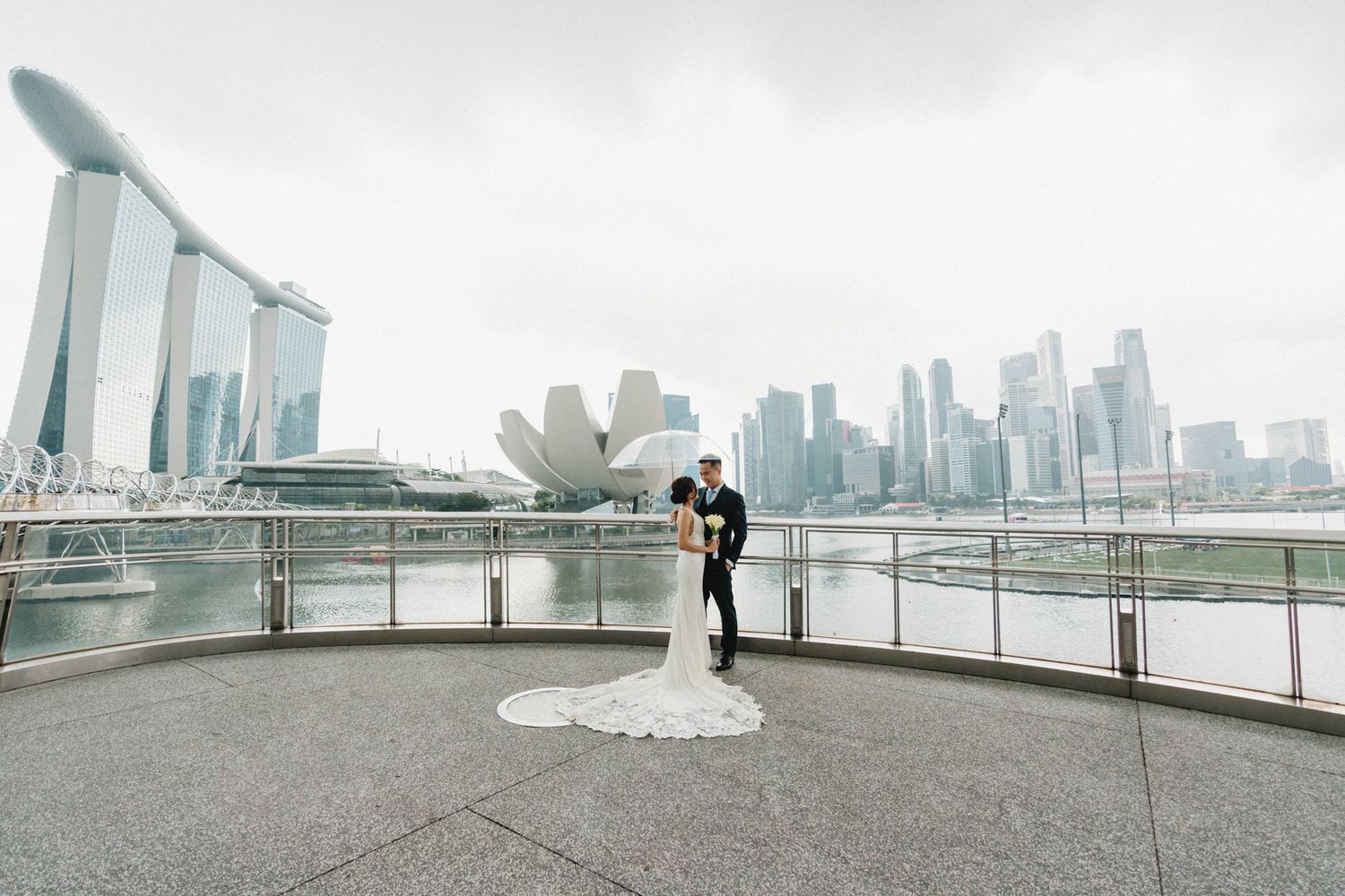Bride and groom share a romantic moment at Marina Bay Sands waterfront with Singapore city skyline backdrop.