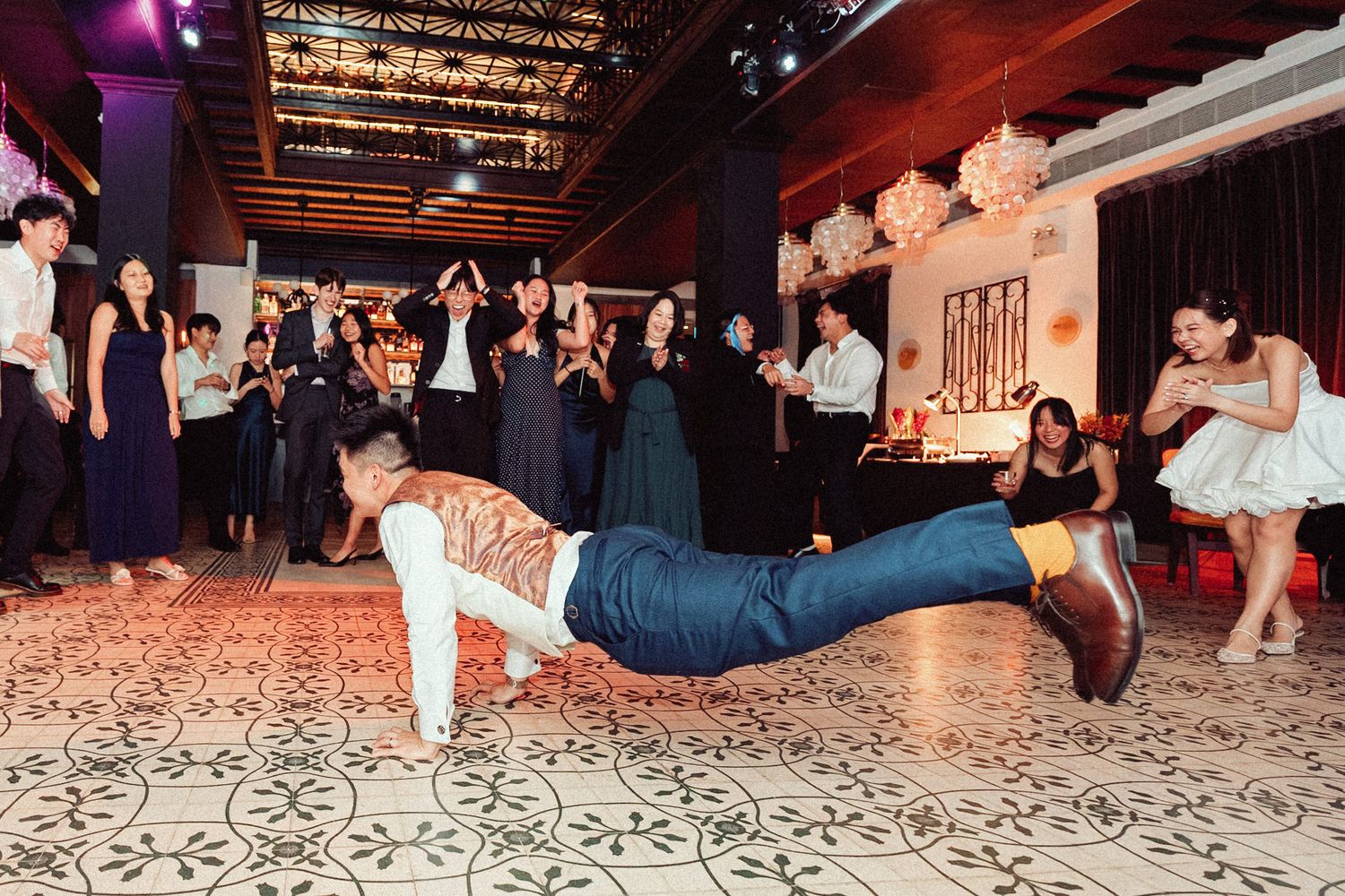 Dancers performing breakdancing moves on a patterned dance floor at an indoor event.