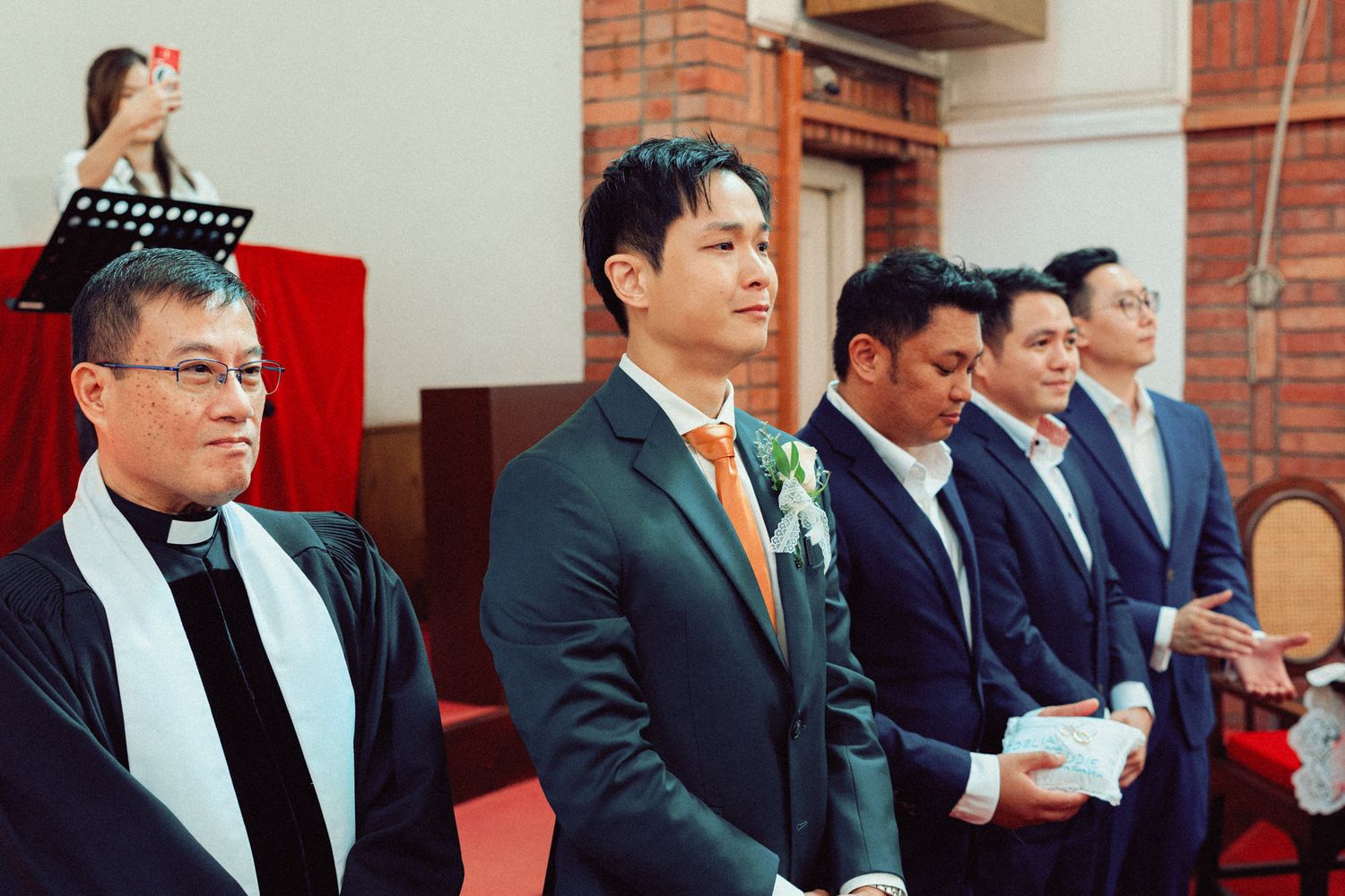 Row of groomsmen in dark suits standing at attention during church ceremony.