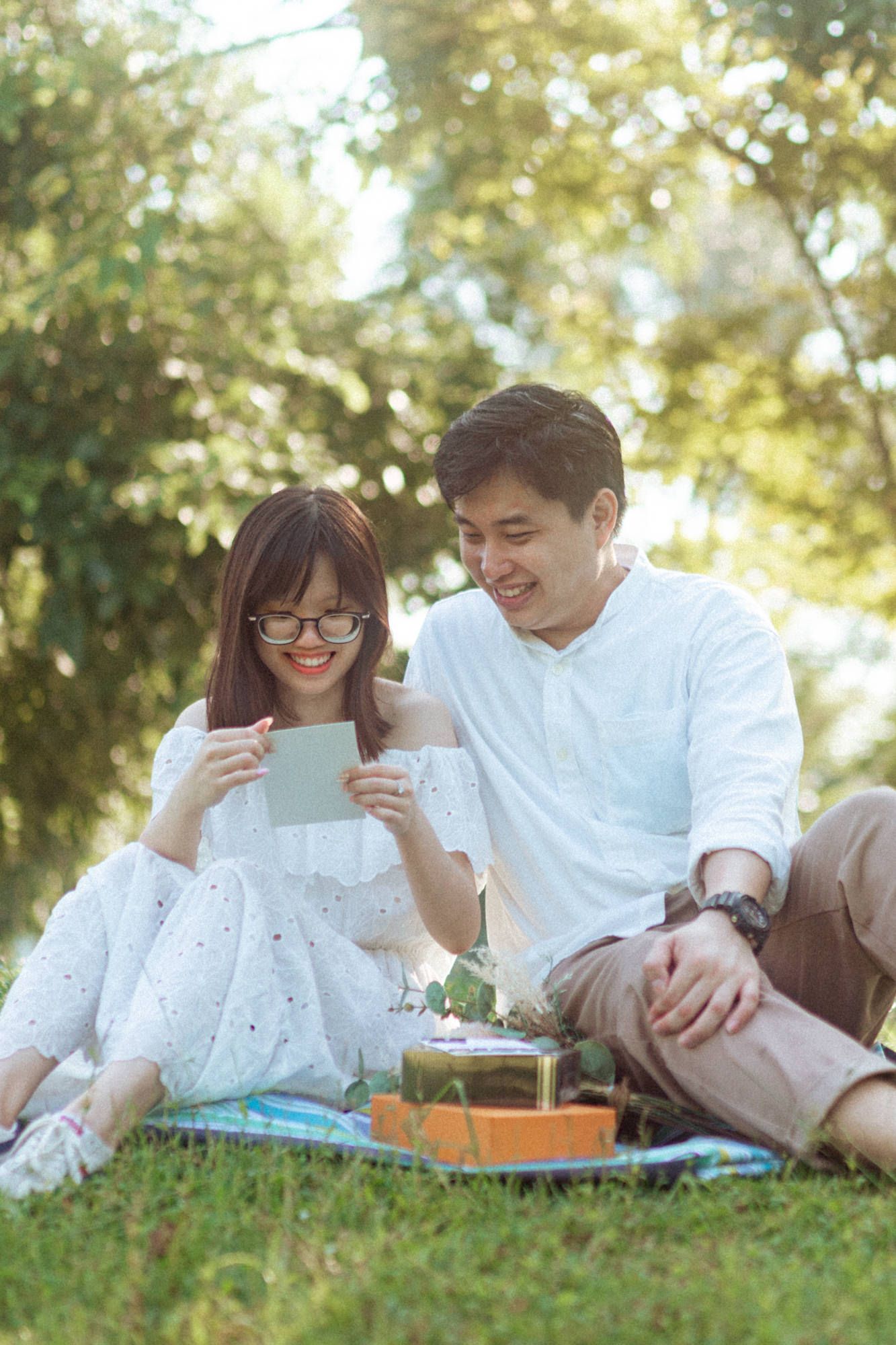 A couple relaxes together on grass while reading books and enjoying a sunny afternoon in the park.