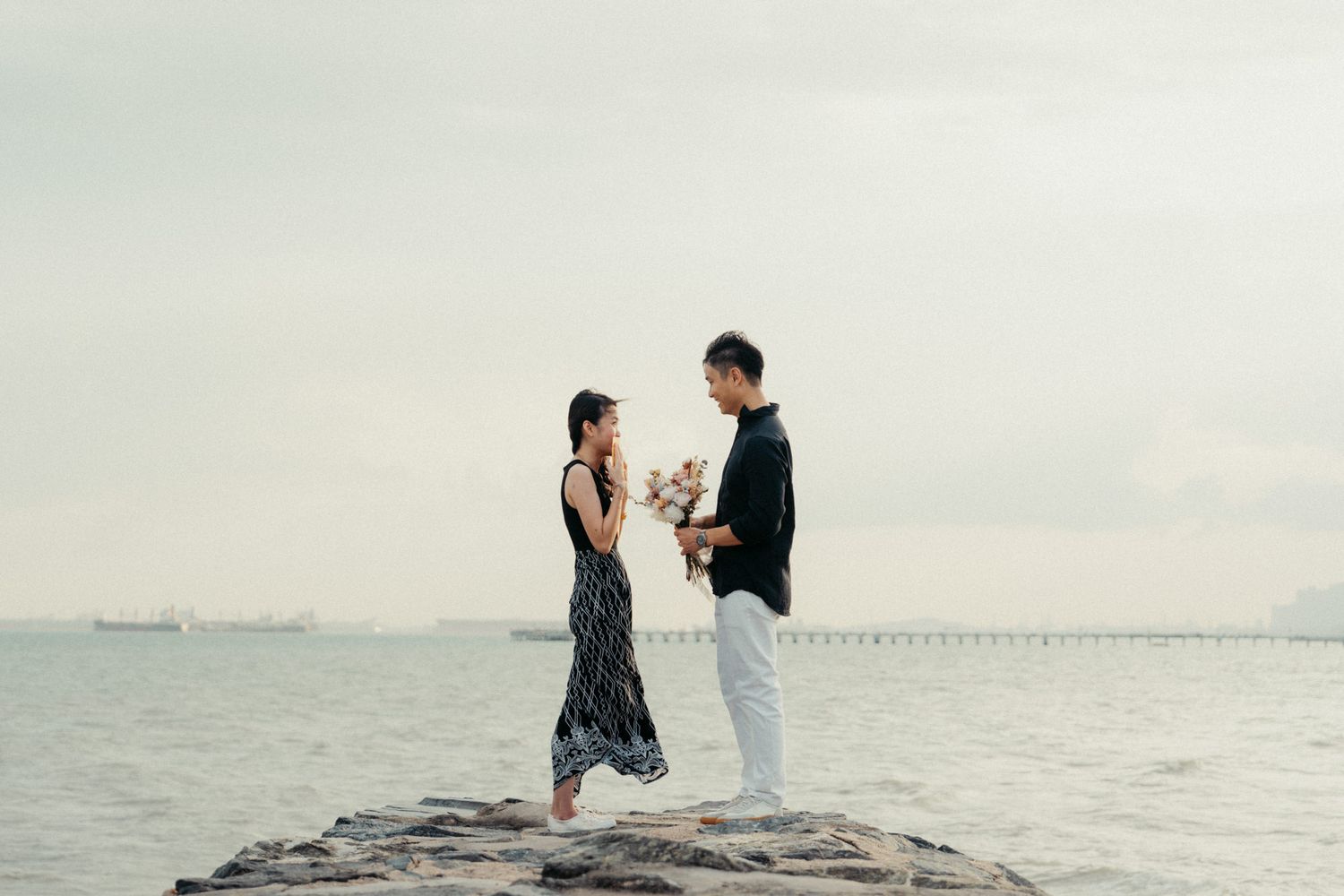 A couple shares a romantic moment on rocky coastal outcrop with ocean view.