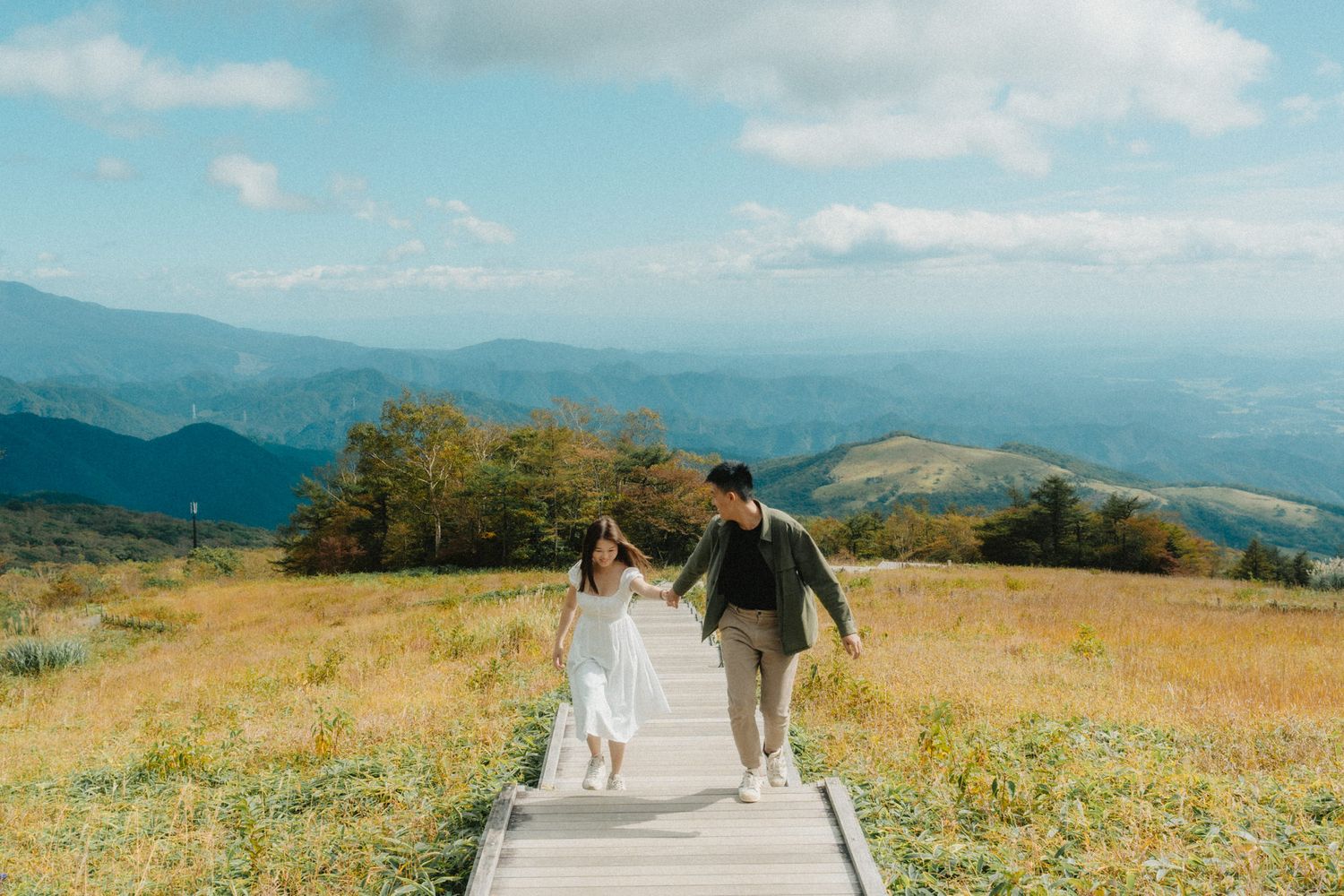 A couple walking hand in hand on a mountain path surrounded by autumn scenery.