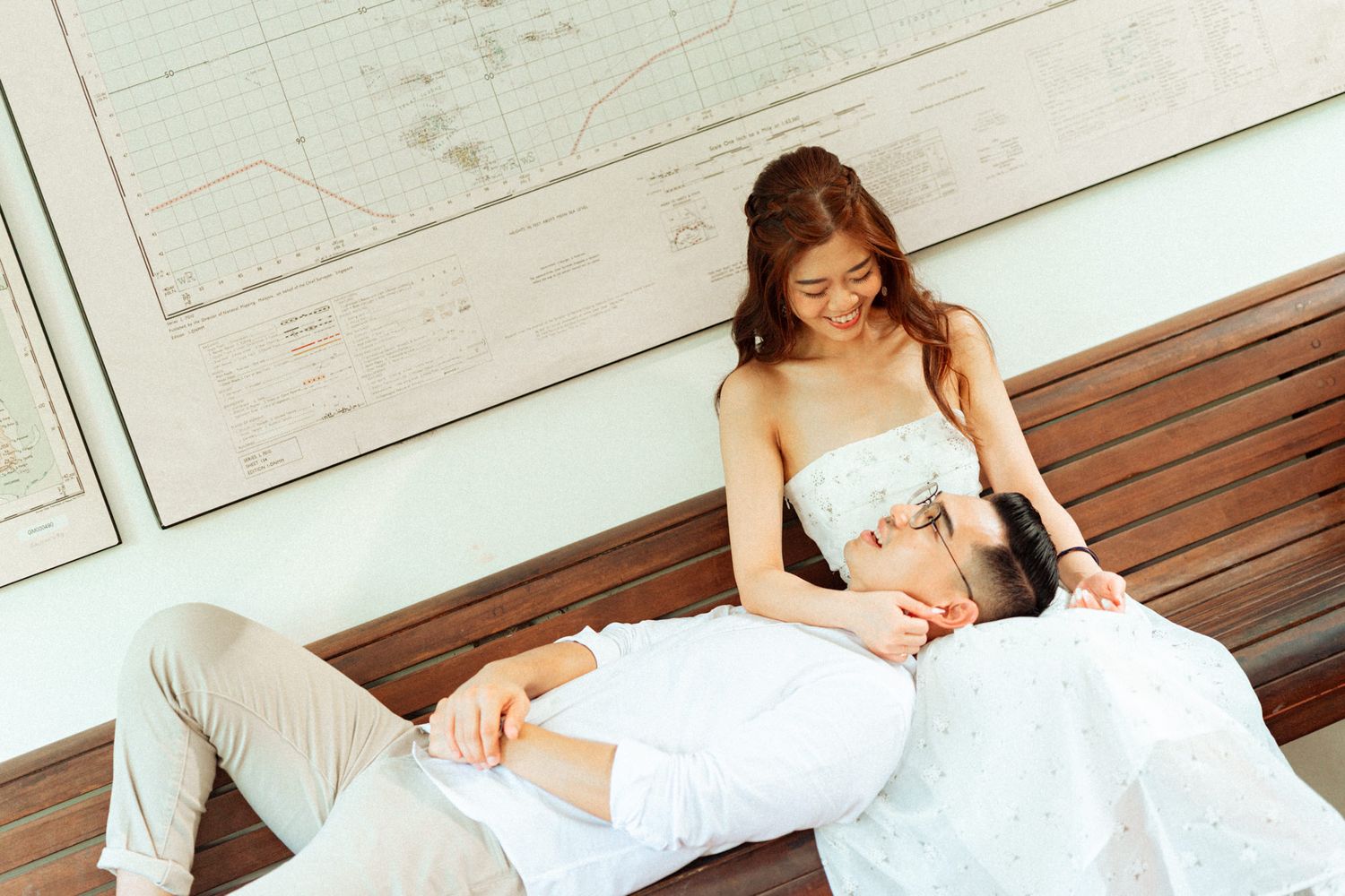 Couple in formal attire pose romantically on wooden deck with white walls.