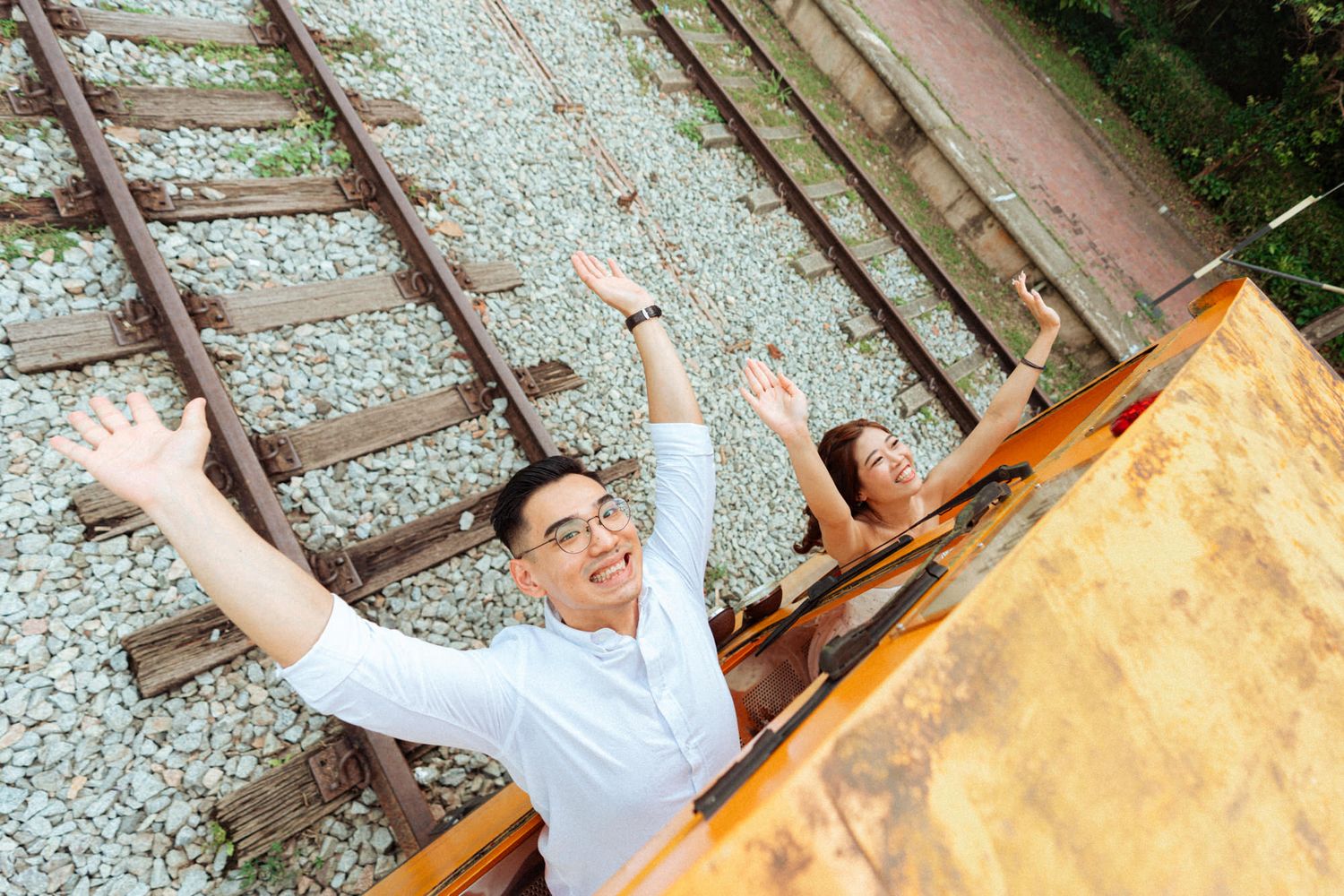 People enjoying a sunny day on vintage railway tracks near an orange rail car.
