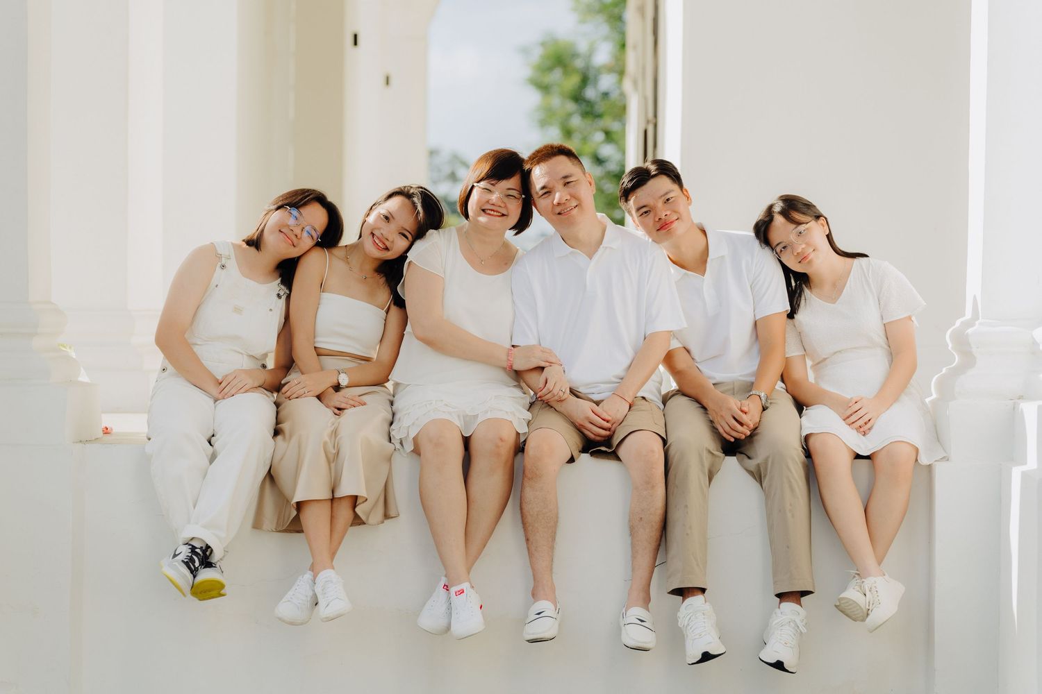 A group of people in white clothing sitting together on a white bench, creating a minimalist aesthetic.