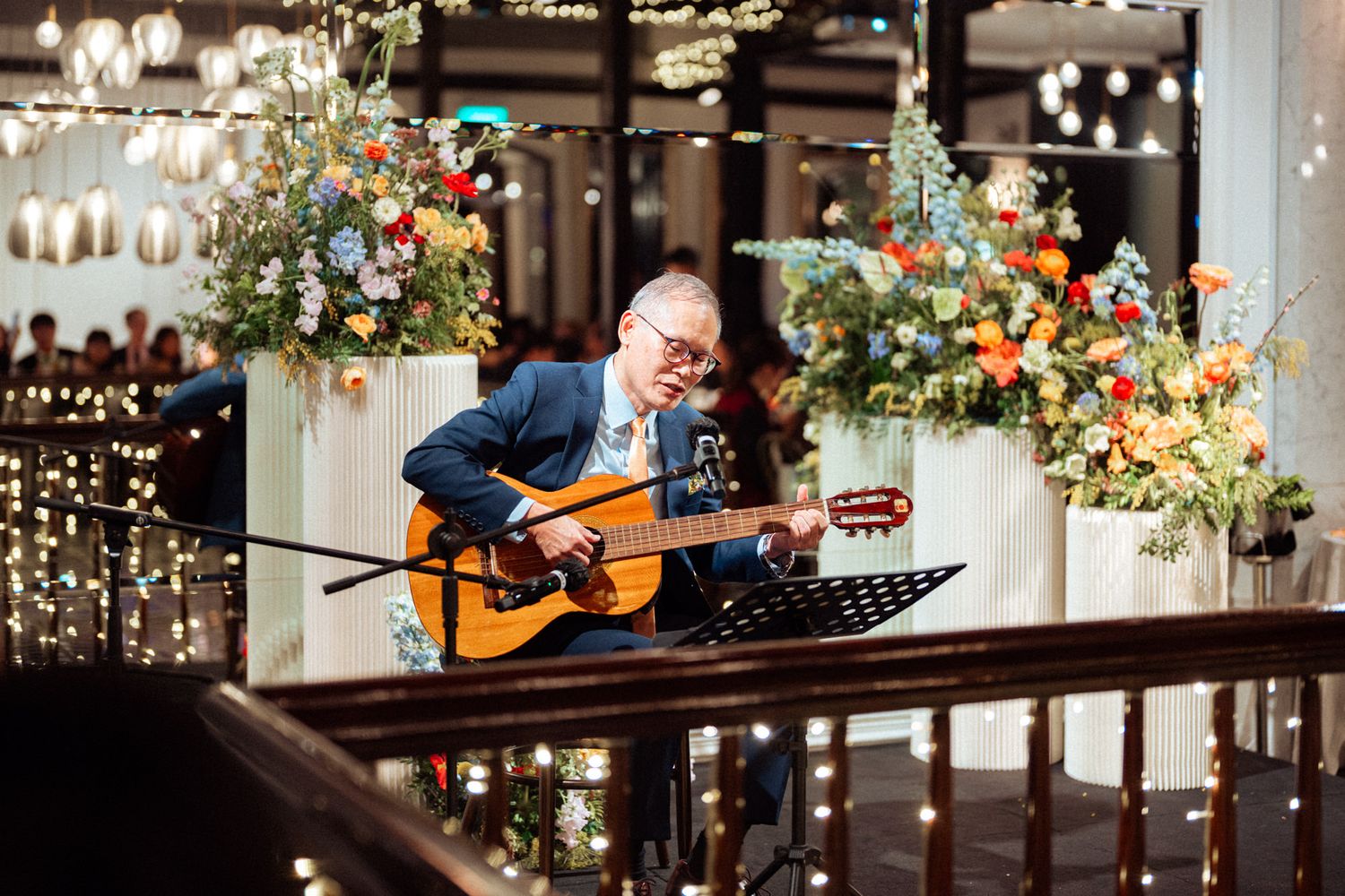 Musician playing acoustic guitar at elegant wedding reception with floral arrangements and fairy lights.