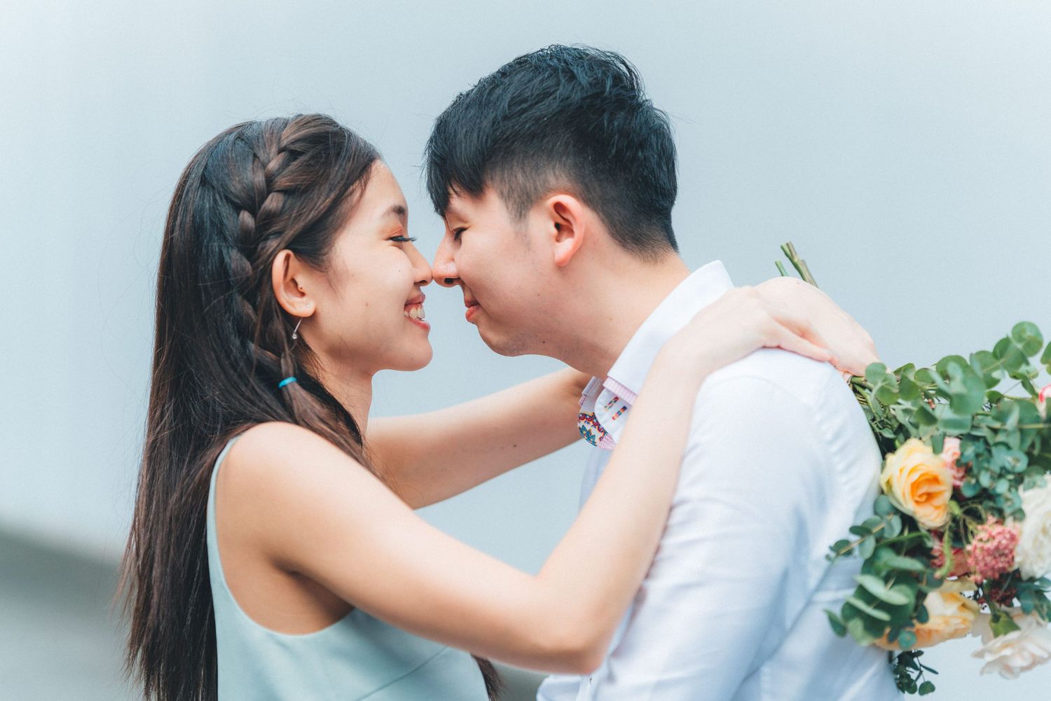 A couple in wedding attire share intimate moments in a bright white studio setting with floral decorations.