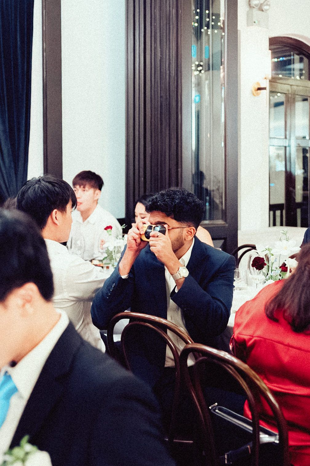 A group of people dining in an elegant restaurant with dark curtains and large windows.