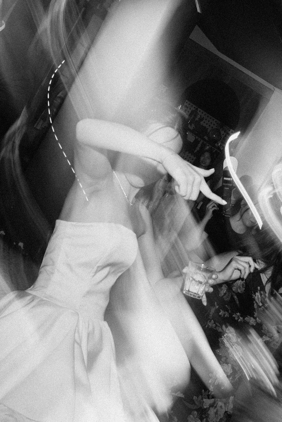 Multiple blurred black and white photos show motion of someone in a white dress dancing at what appears to be a celebration.