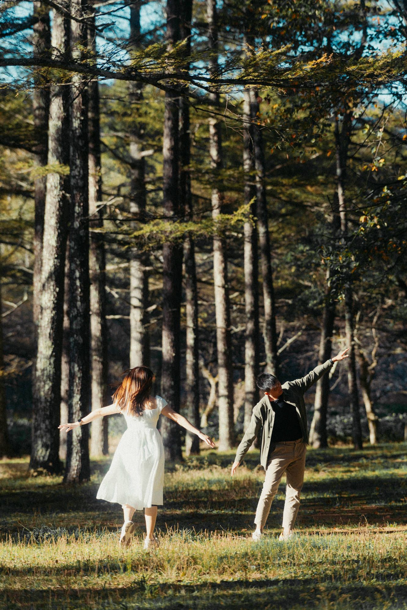 Two people dancing joyfully in a pine forest clearing.