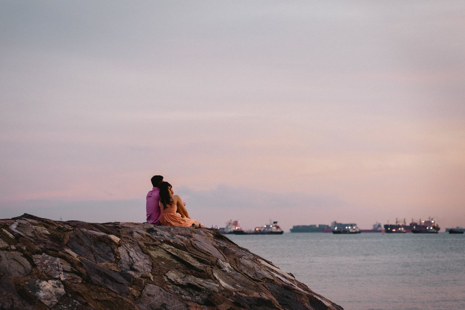 Romantic couple walking along the shoreline at dusk in coordinated pastel outfits.