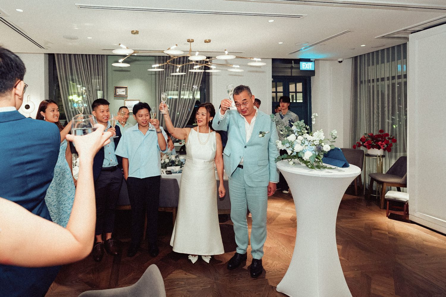 A couple celebrates at their wedding reception in a modern venue with guests cheering in the background.