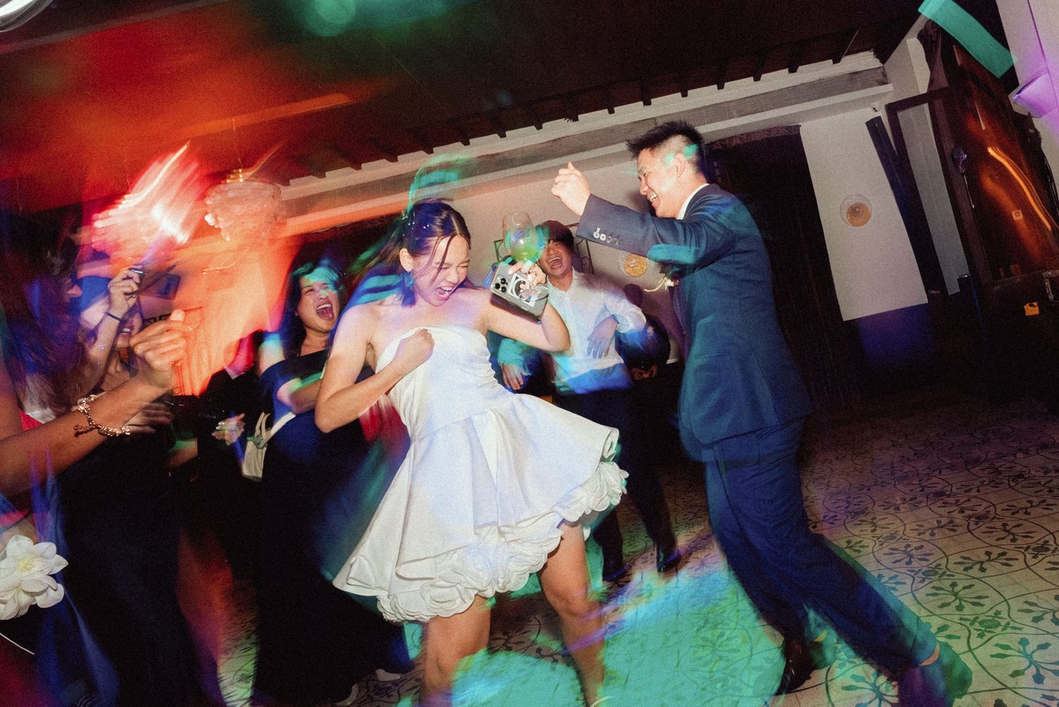 People dancing together at a wedding reception with colorful lighting and decorations on the dance floor.