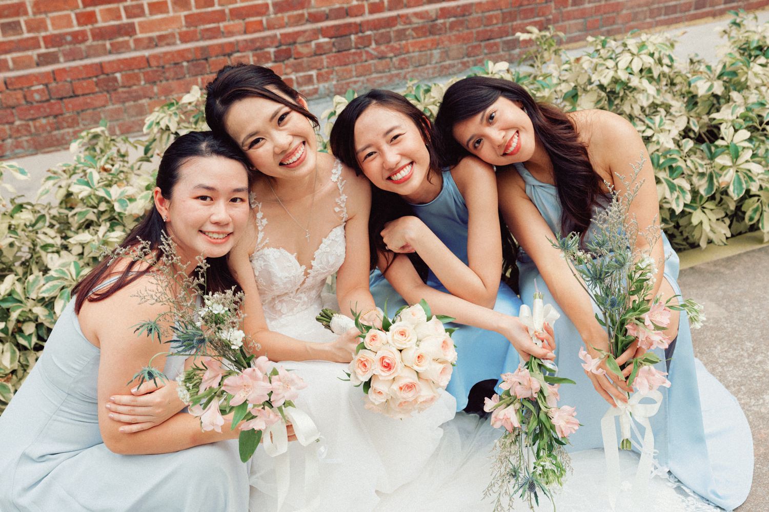 Bridal party in powder blue dresses laughing together against brick backdrop.