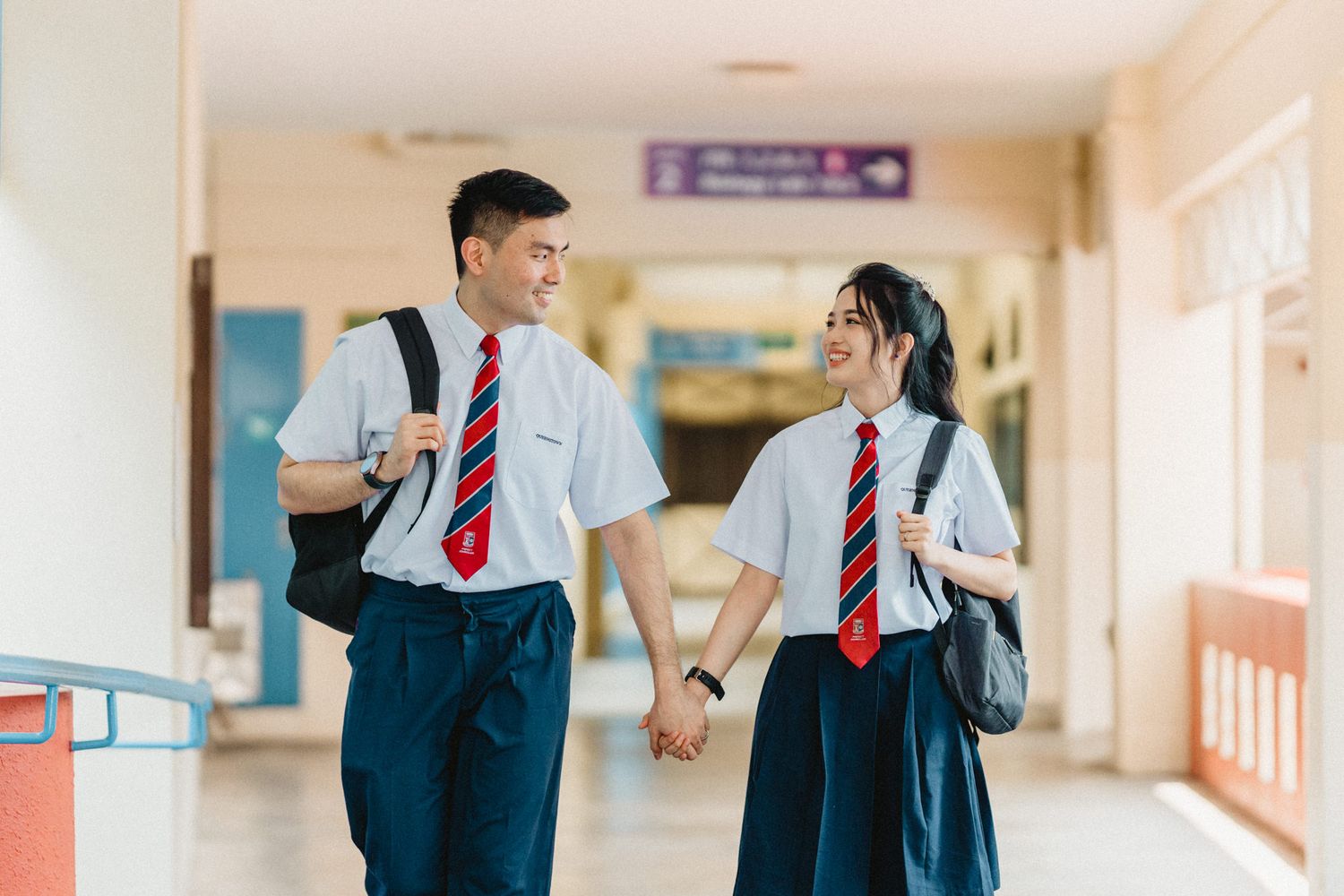 Students in matching uniforms holding hands while walking down a school corridor.