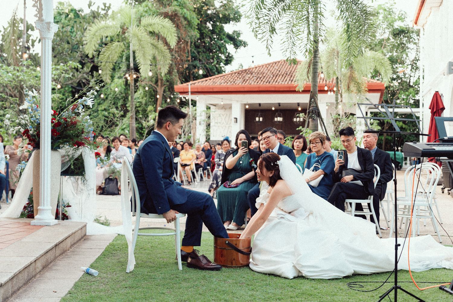 Wedding ceremony setup outdoors with white chairs and decorations under trees at a garden venue.