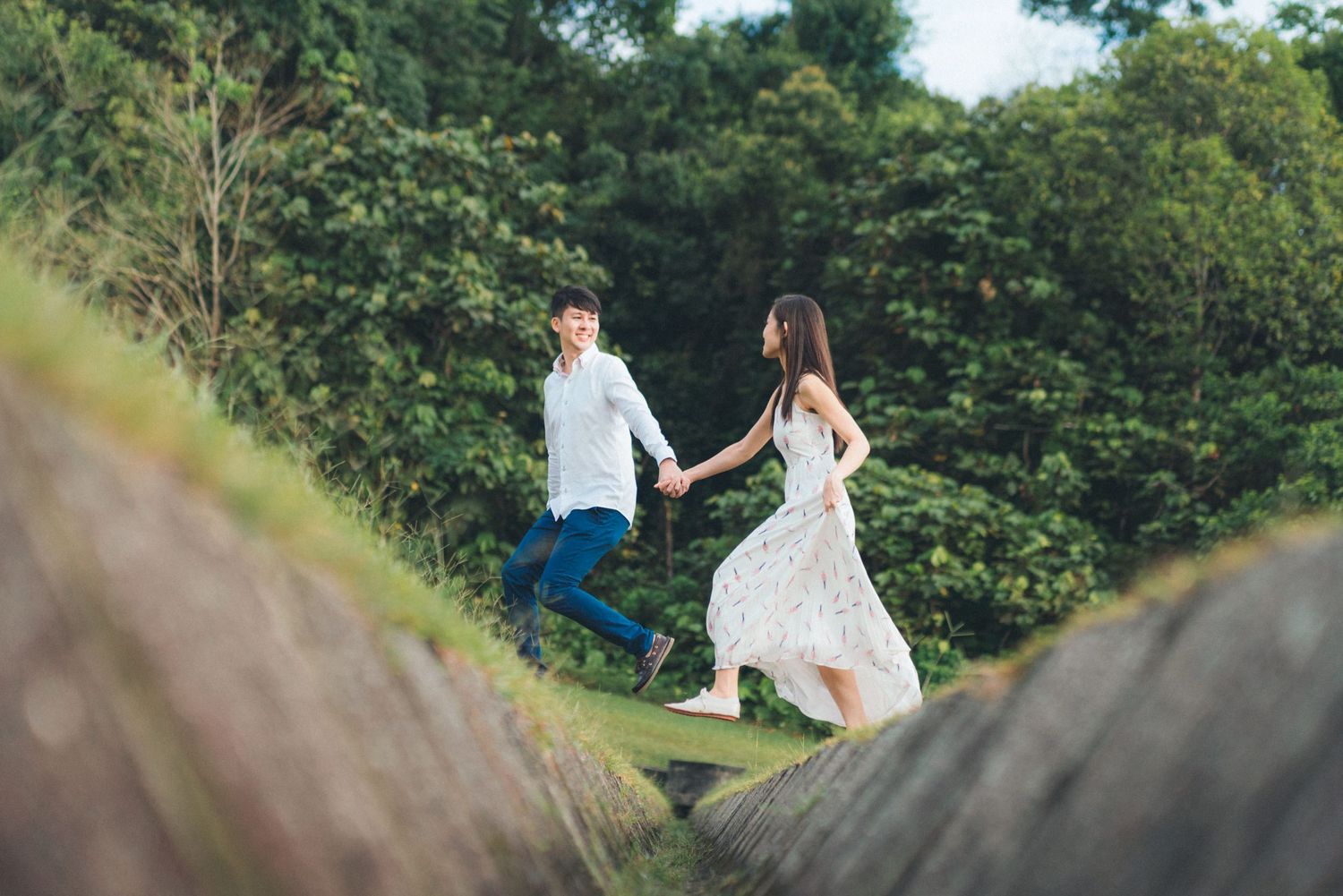 A couple in wedding attire walks through a lush green field during a romantic outdoor photoshoot.
