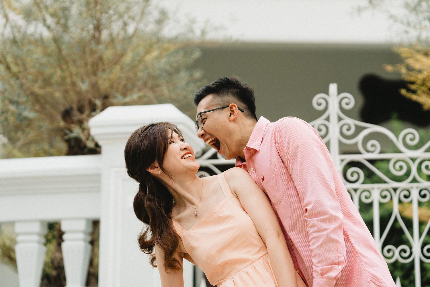 A romantic couple poses together against a white colonial-style balcony with decorative railings.