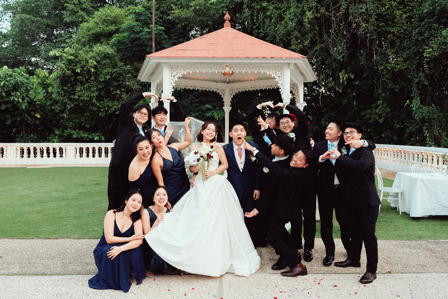 A wedding party poses on the lawn in front of a white gazebo during an elegant outdoor celebration.
