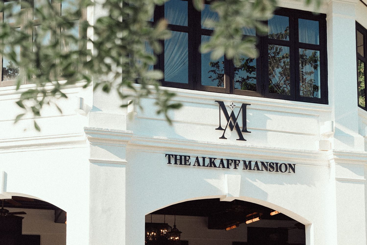 The Alkaff Mansion's elegant white colonial facade stands prominently against lush greenery in Singapore.