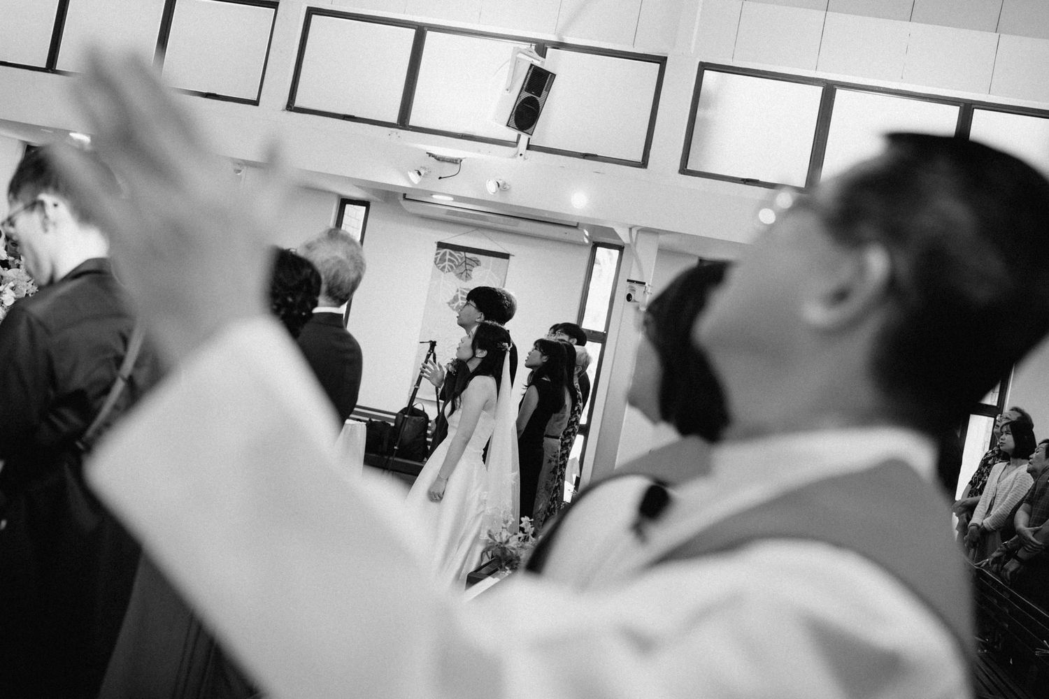 Black and white photo of a priest raising his hand during a wedding ceremony in a church.