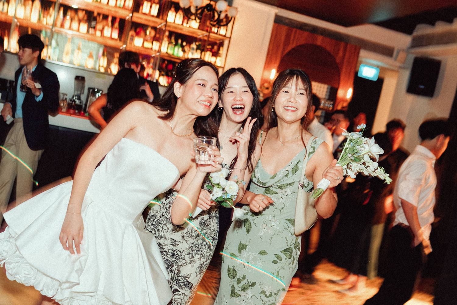 Group of people celebrating and socializing at a dimly lit bar with warm lighting and festive atmosphere.