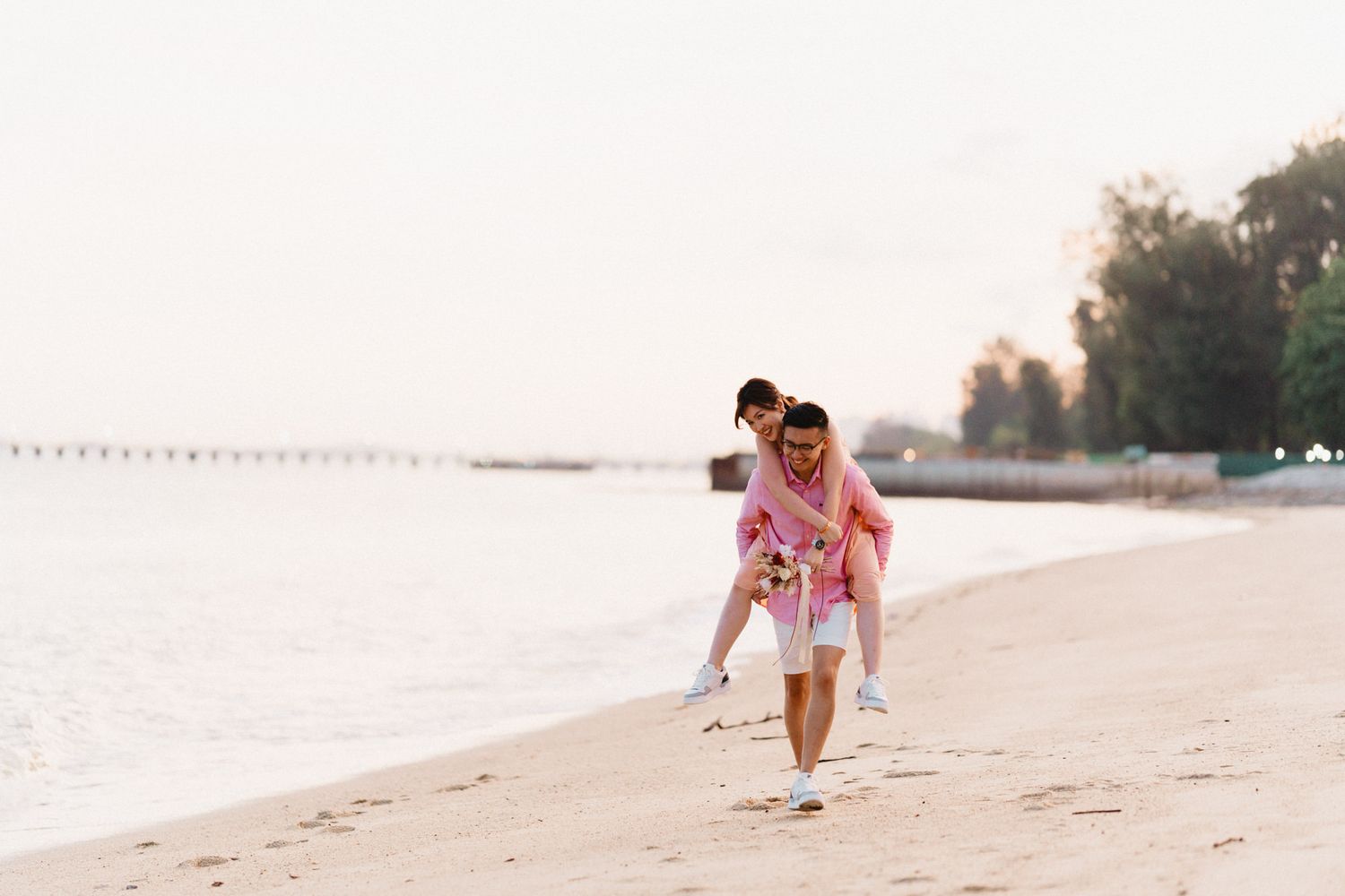 Couple enjoying playful moments on a sandy beach during golden hour.