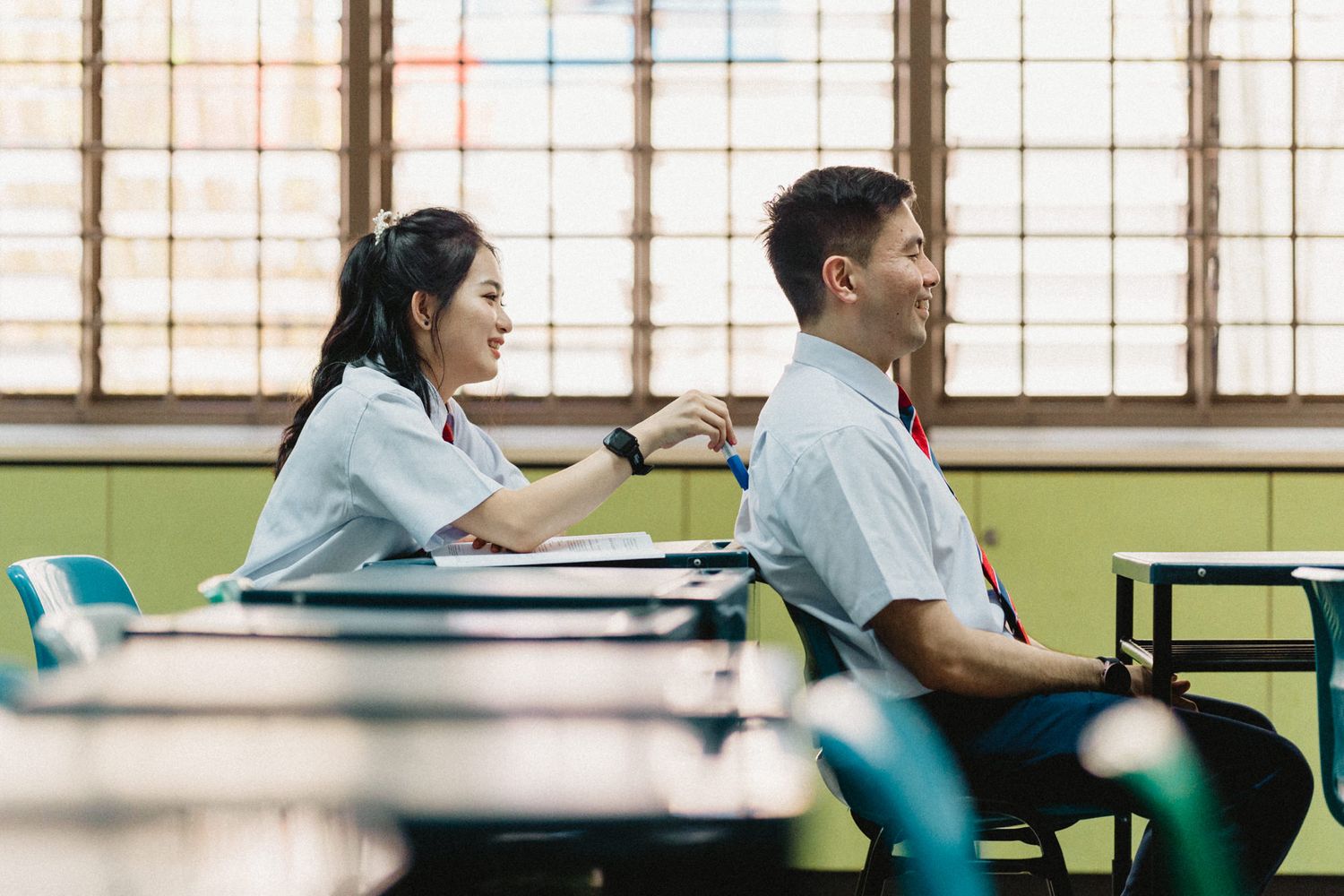 Students in school uniforms studying at desks in a bright classroom setting.