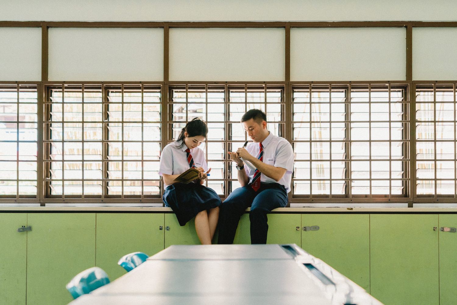 Students studying together in a classroom with large windows and green walls.