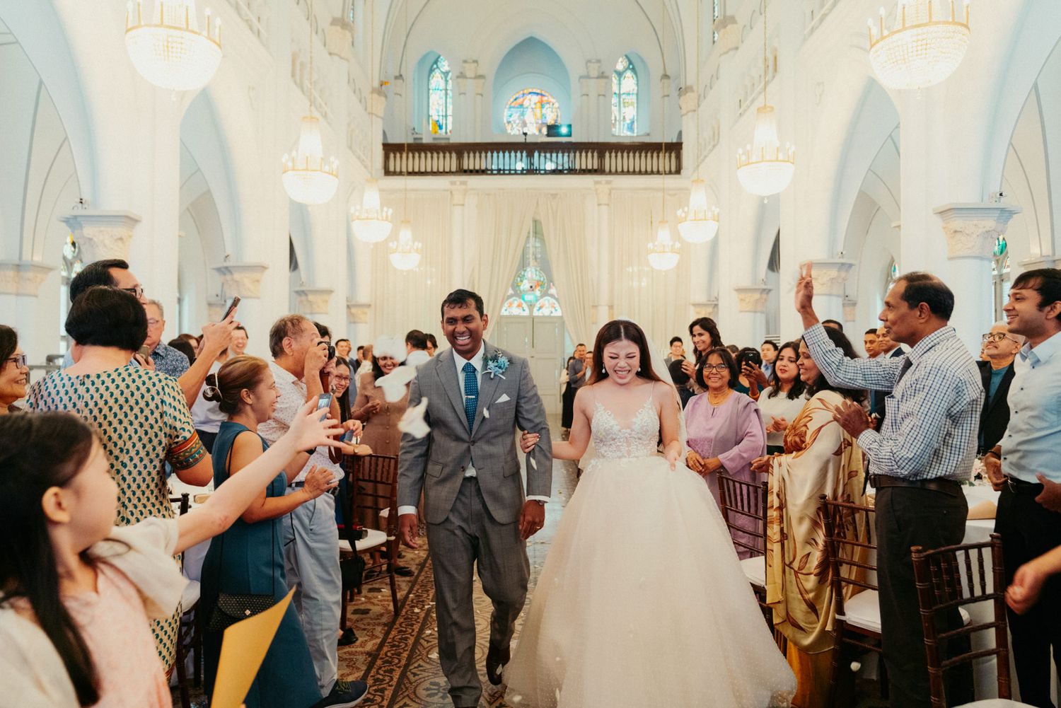 Joyful newlyweds walk down church aisle as guests celebrate their wedding ceremony with confetti.