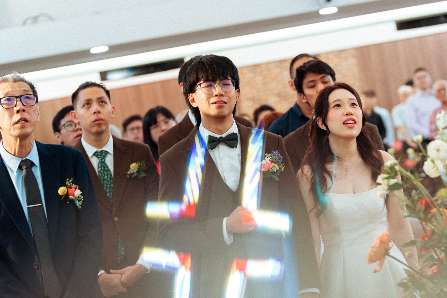 Bride and groom stand together during wedding ceremony in church, surrounded by guests in formal attire.