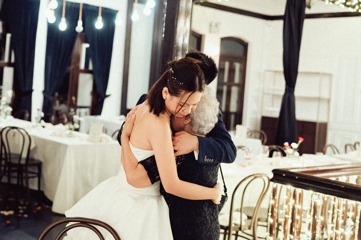 A couple shares a tender moment during their wedding reception while seated at an elegantly decorated table.