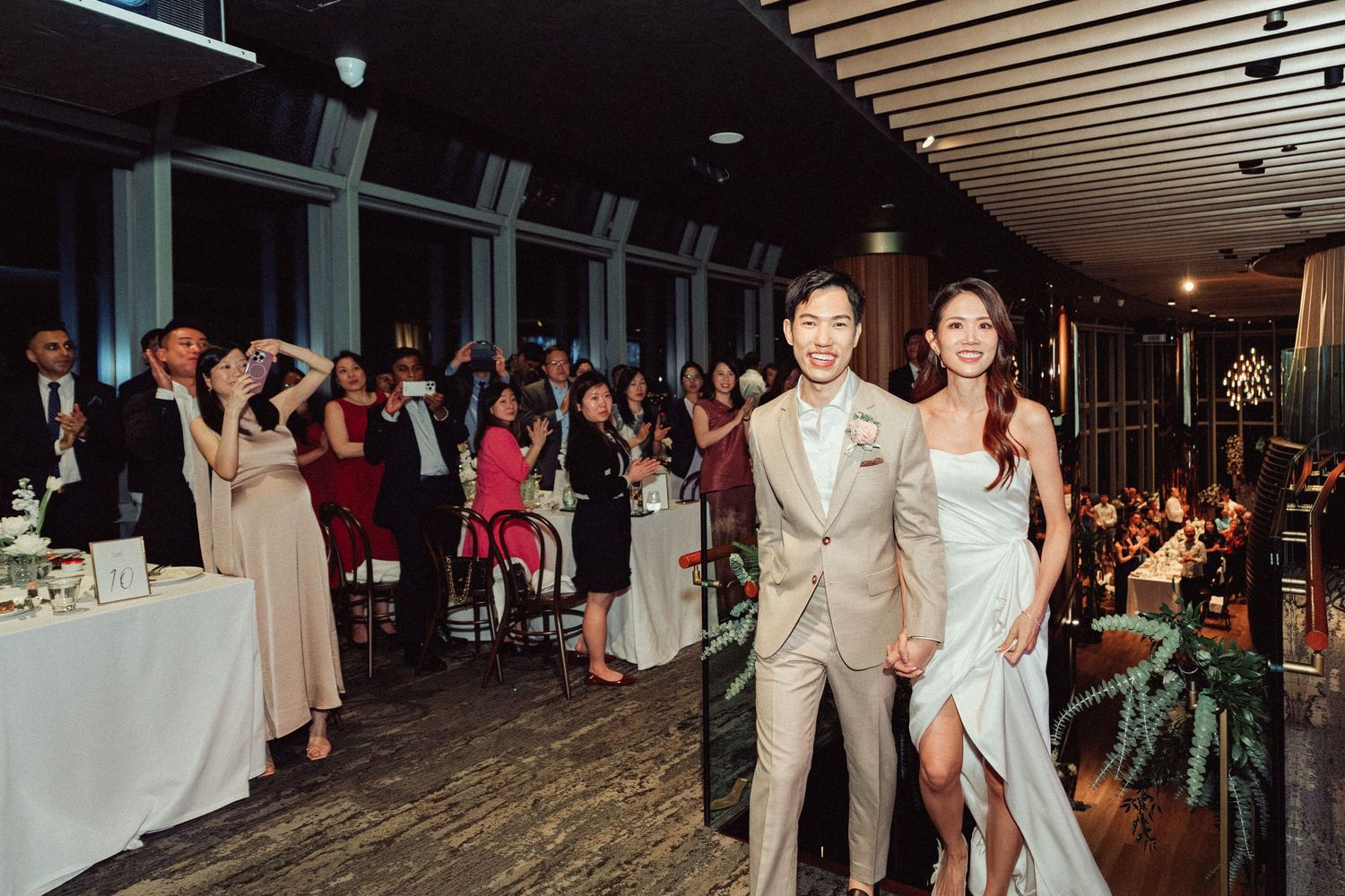 Newlyweds make their entrance at a wedding reception as guests cheer in the background.