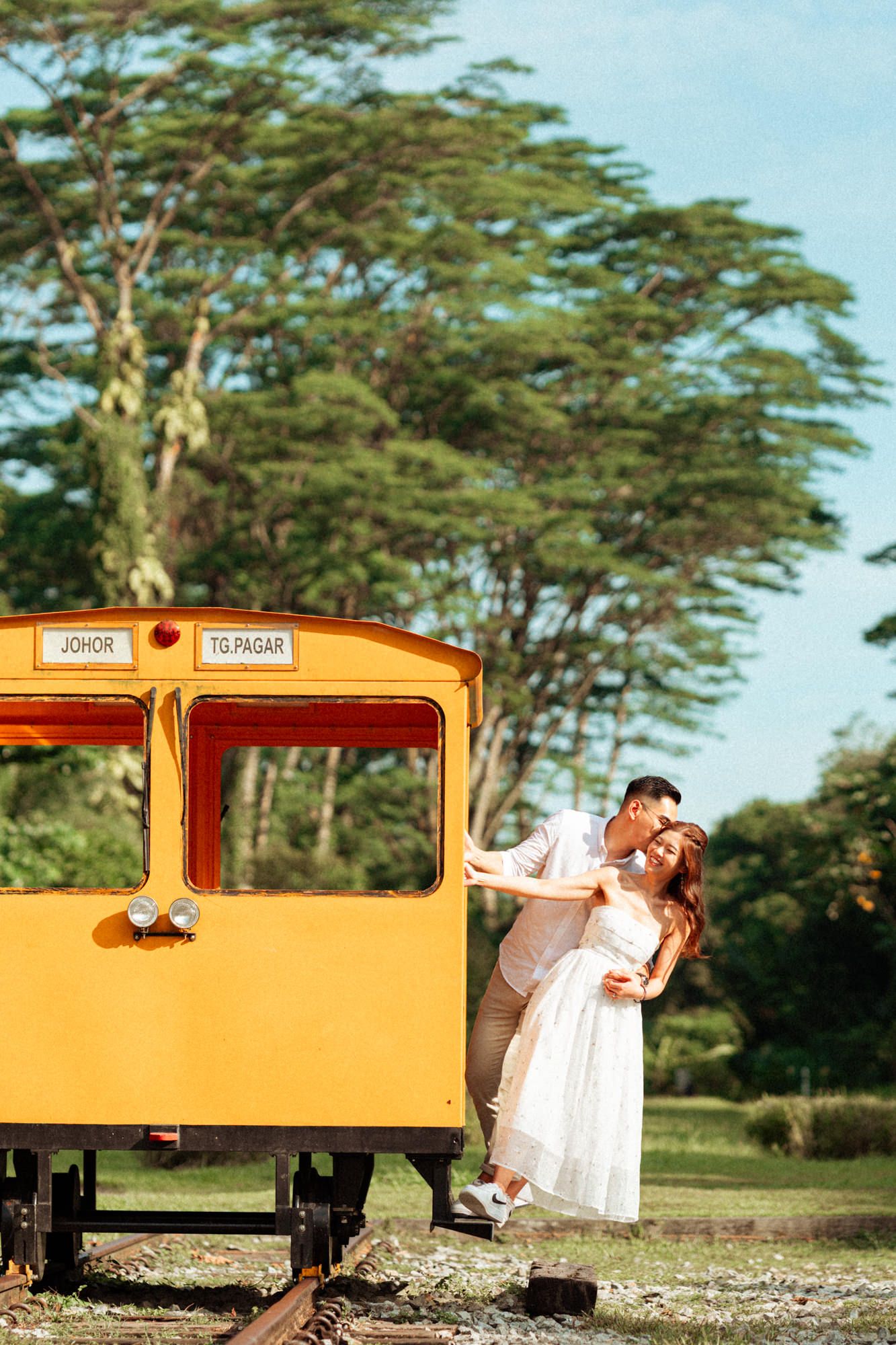 Vintage orange train car parked on tracks surrounded by tropical trees.
