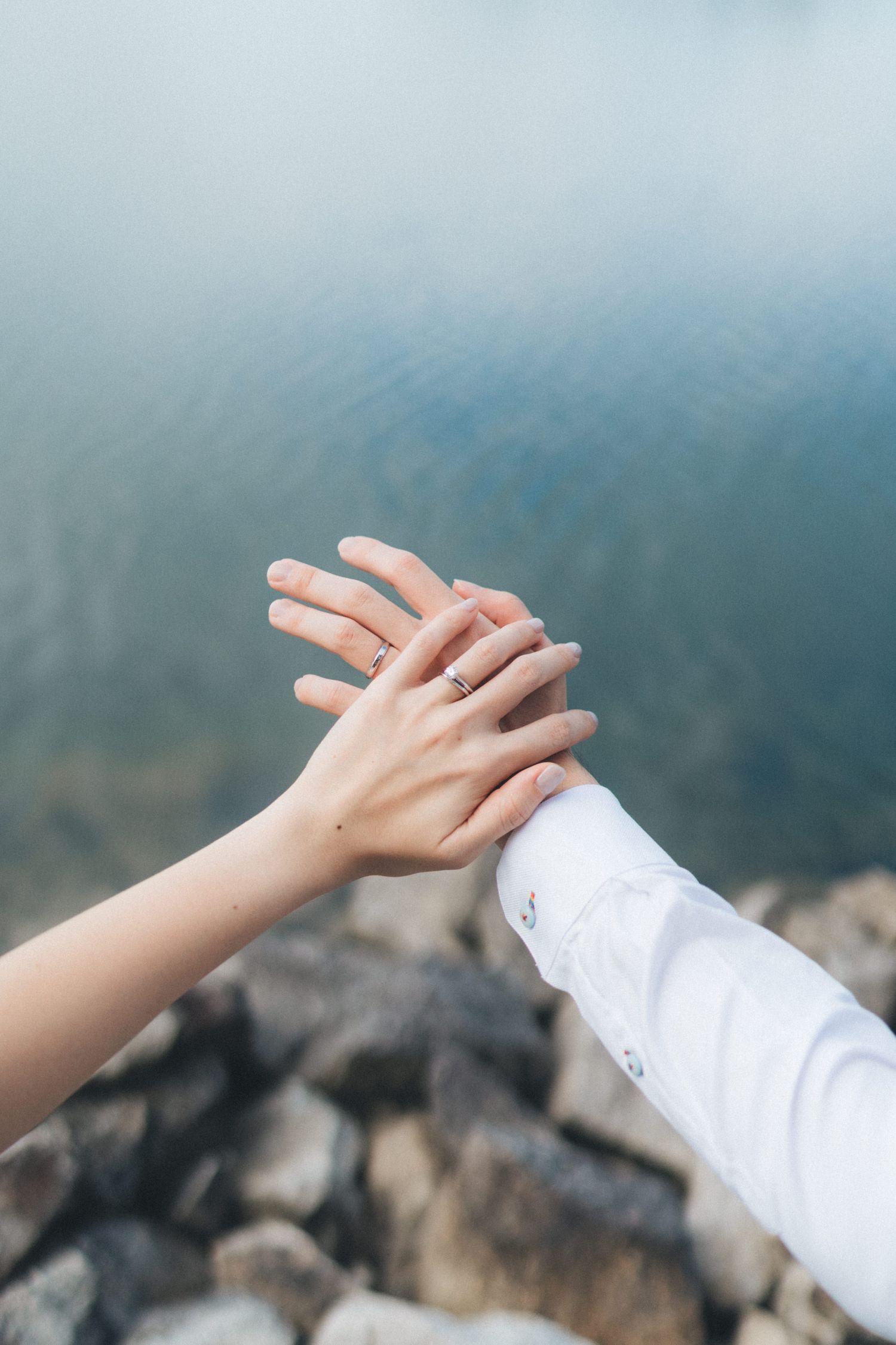 Two hands reach out towards each other against a blurred mountain landscape backdrop in an artistic composition.