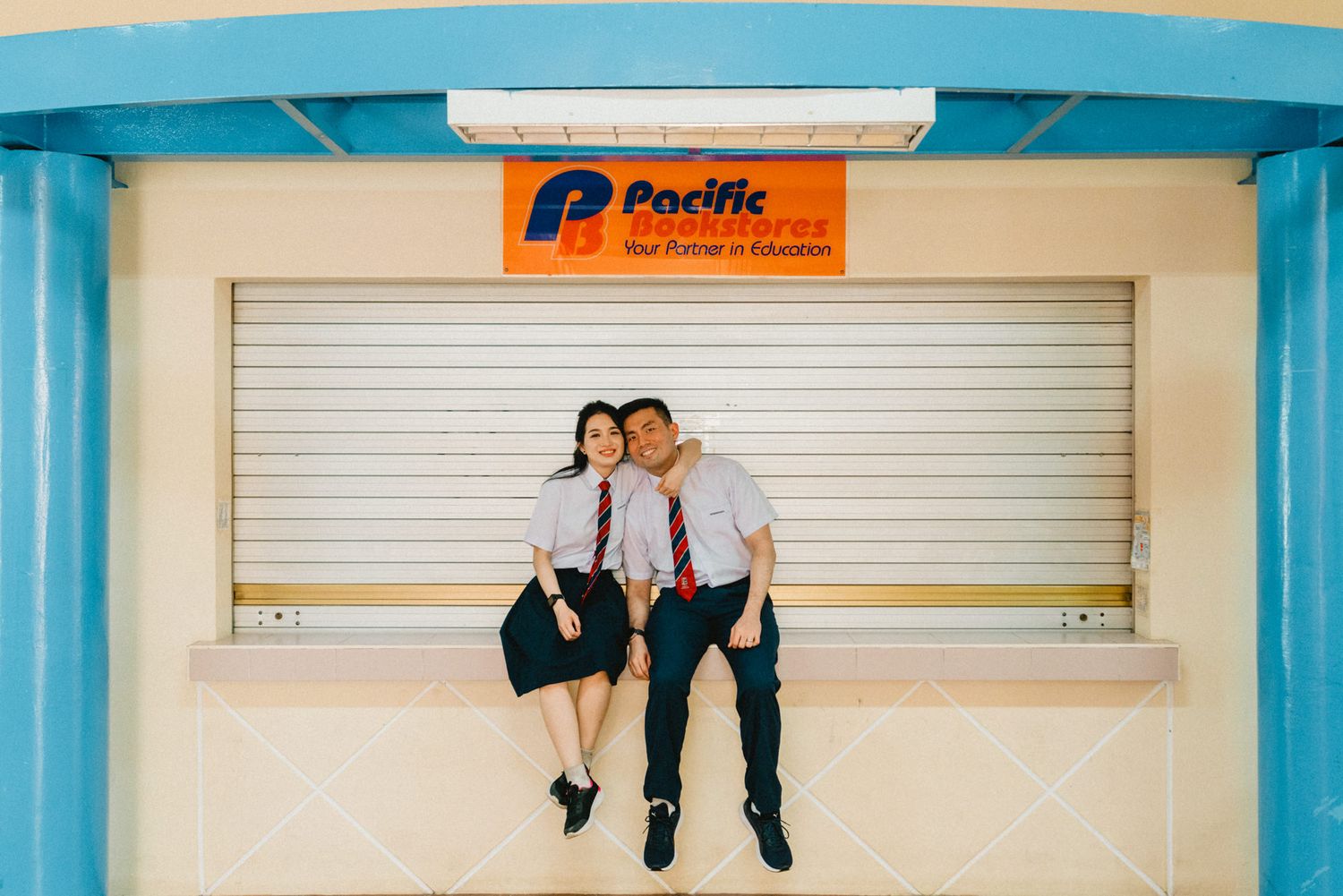 Students in uniforms sitting together on a blue and white storefront with Pacific signage.
