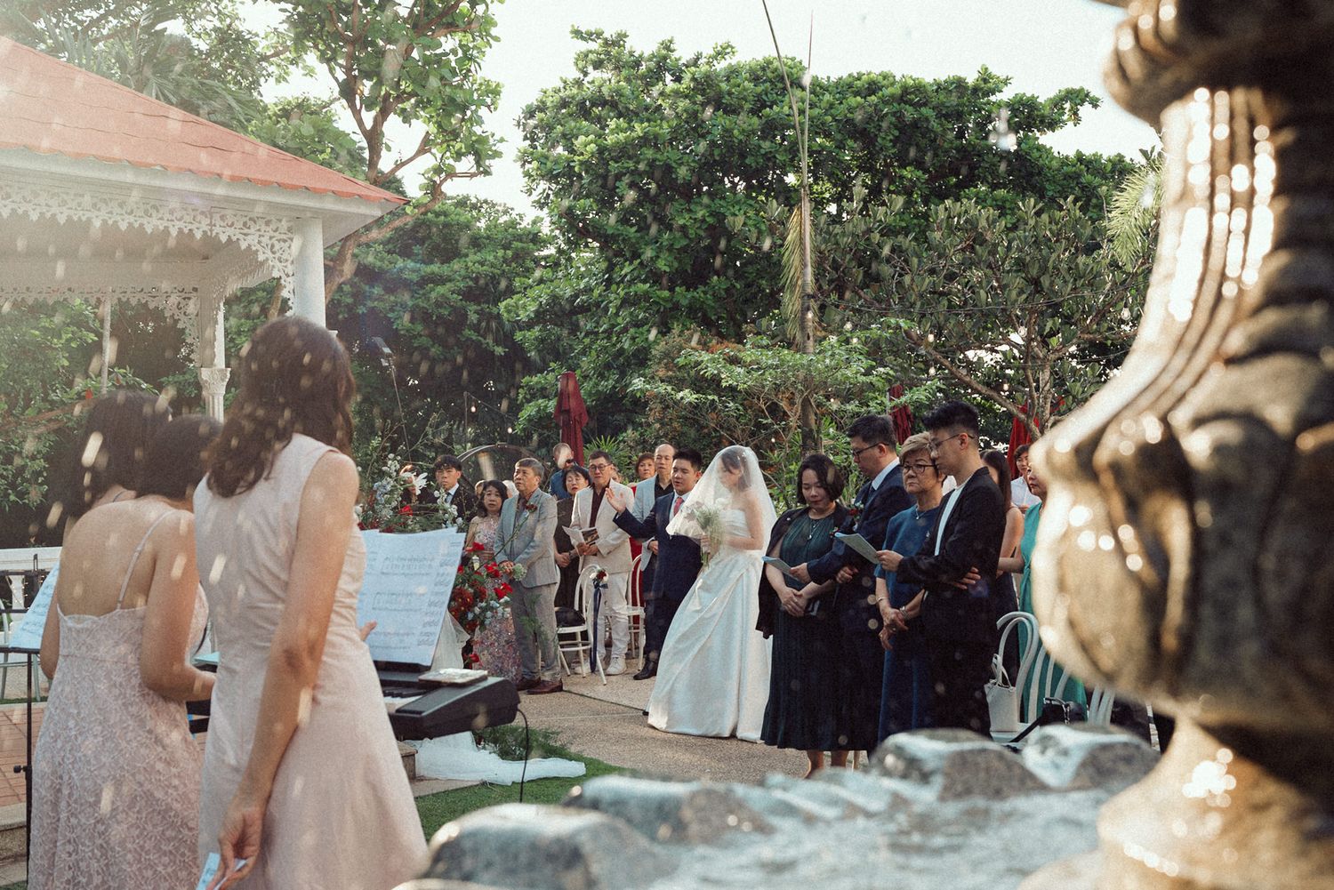 Wedding guests gather outdoors at dusk for a celebration with string lights illuminating the garden venue.