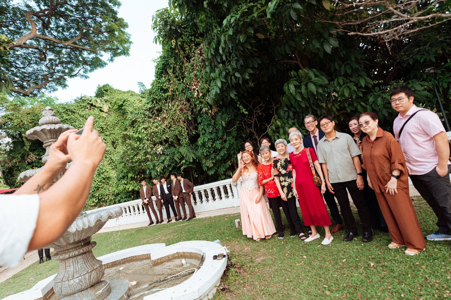 Group of people posing for a photo outdoors in a lush garden during a formal celebration or wedding event.