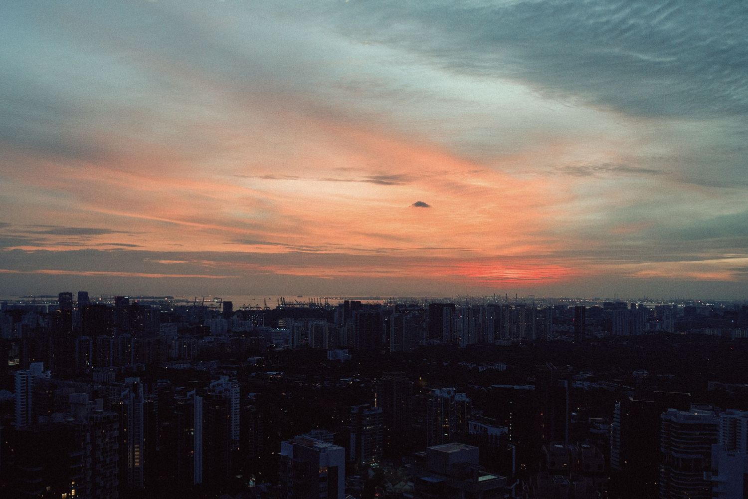 Panoramic sunset cityscape view with orange and blue sky over urban buildings.