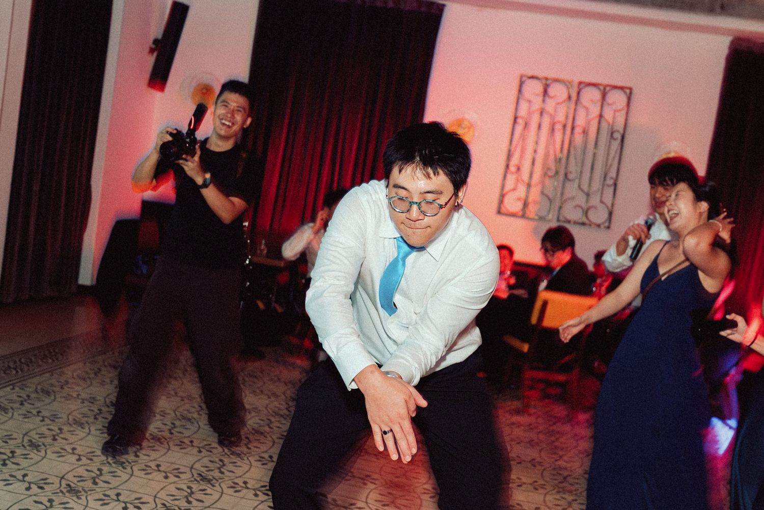 People dancing together at a dimly lit venue with red lighting and dark interior decor.