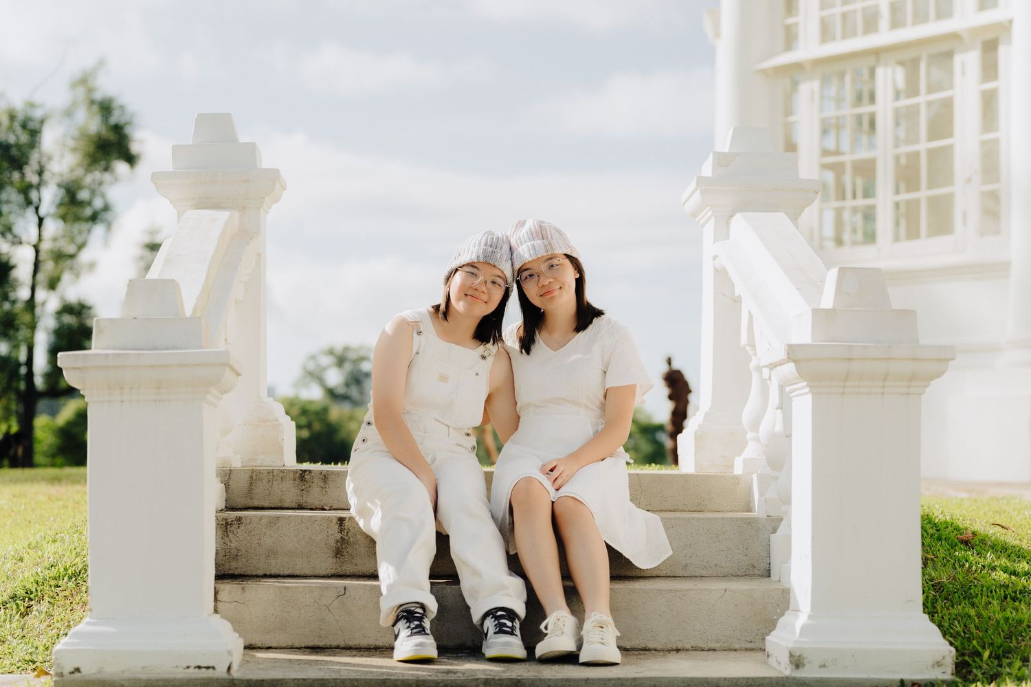 A couple sits together on white stone steps outdoors during a sunny engagement photo session.