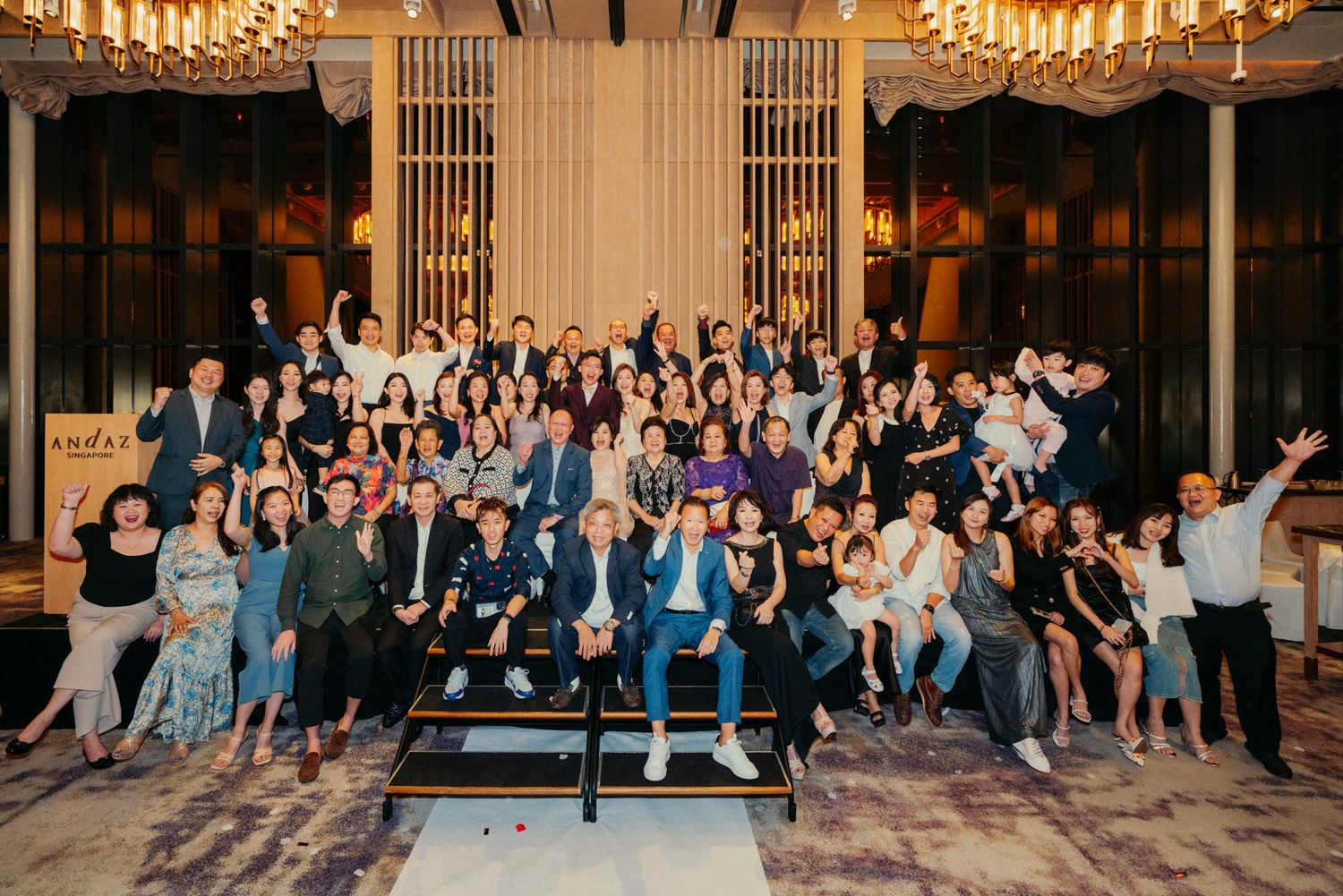 Large group photo of elegantly dressed guests celebrating at a formal event in a luxurious ballroom.