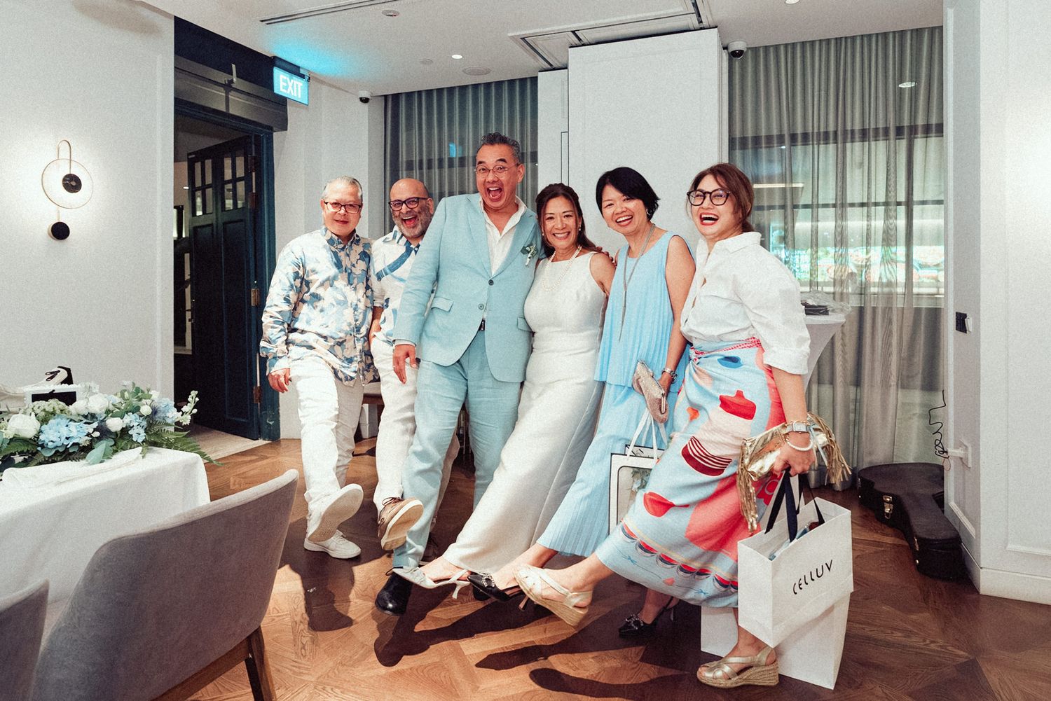 A group wearing light blue and white attire poses together in a bright modern interior space.
