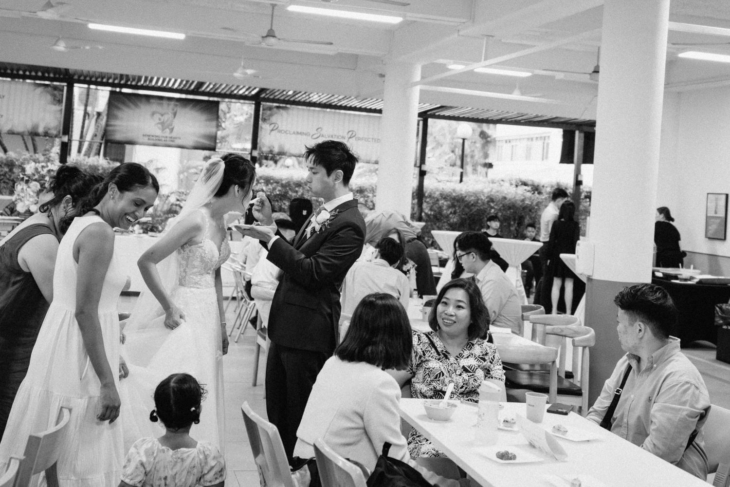 A black and white reception scene showing guests celebrating at tables.