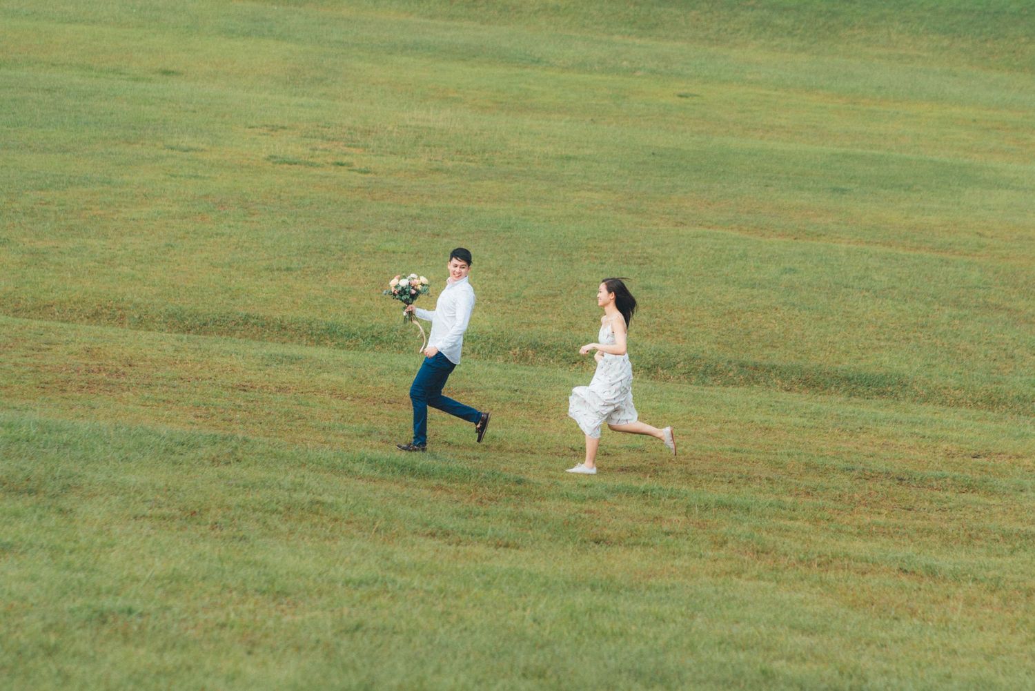 People in white outfits running and playing together on a vast green grassy field on a sunny day.
