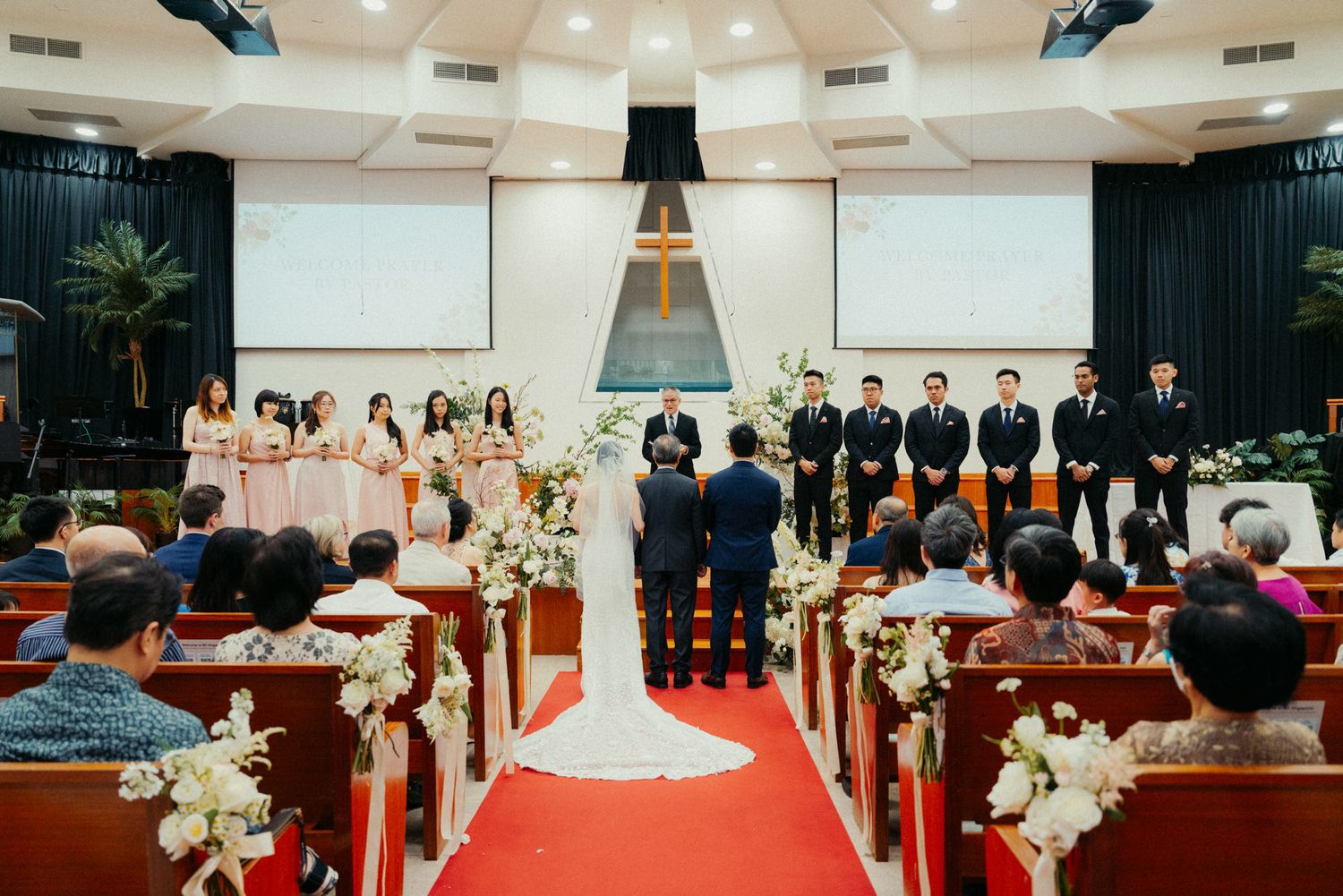 Elegant church wedding ceremony with bride and groom at altar, bridal party, and seated guests in decorated chapel.