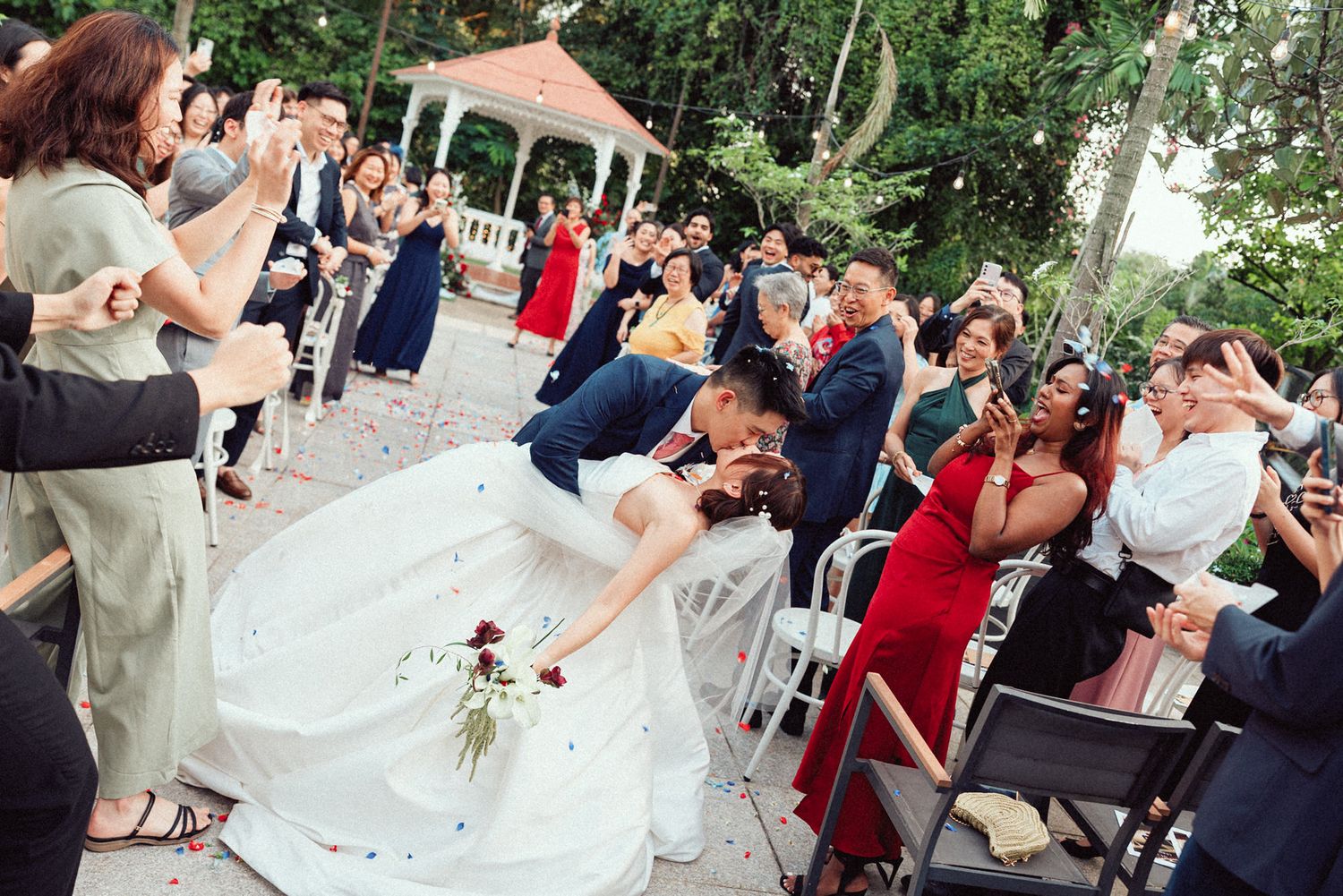 Wedding guests raise their glasses in a celebratory toast during an outdoor garden reception.