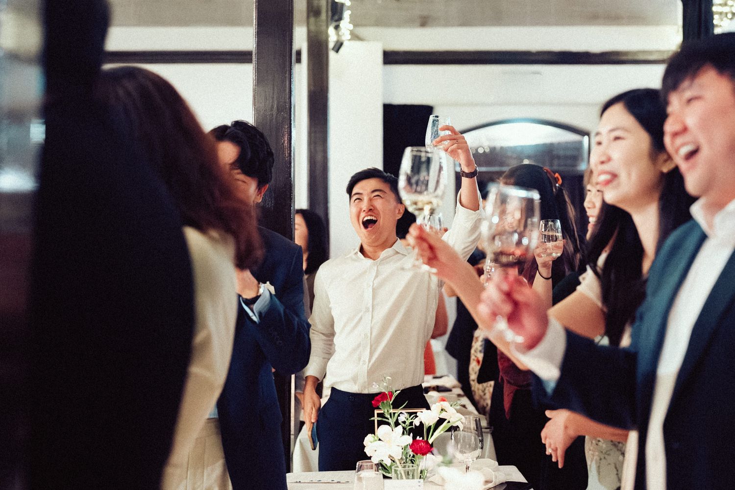Wedding guests celebrate and laugh together during a joyful reception party at an indoor venue.